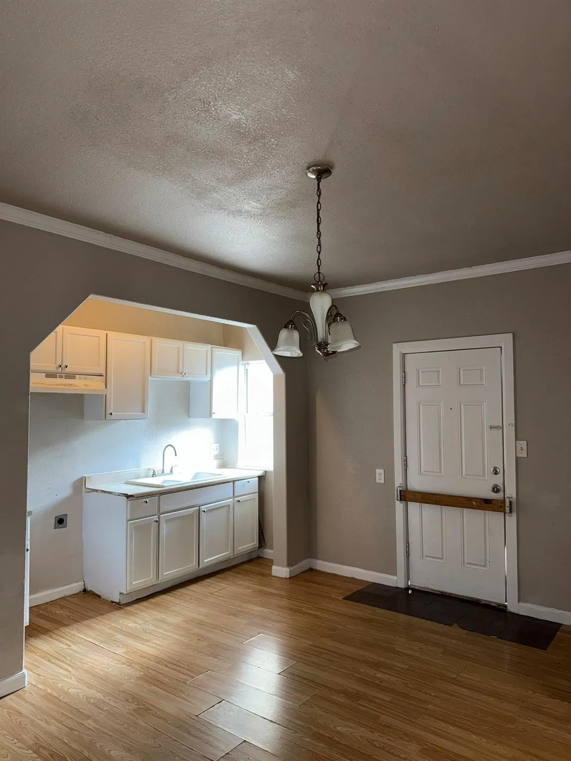 Kitchen featuring crown molding, light countertops, light wood finished floors, white cabinetry, and hanging lights
