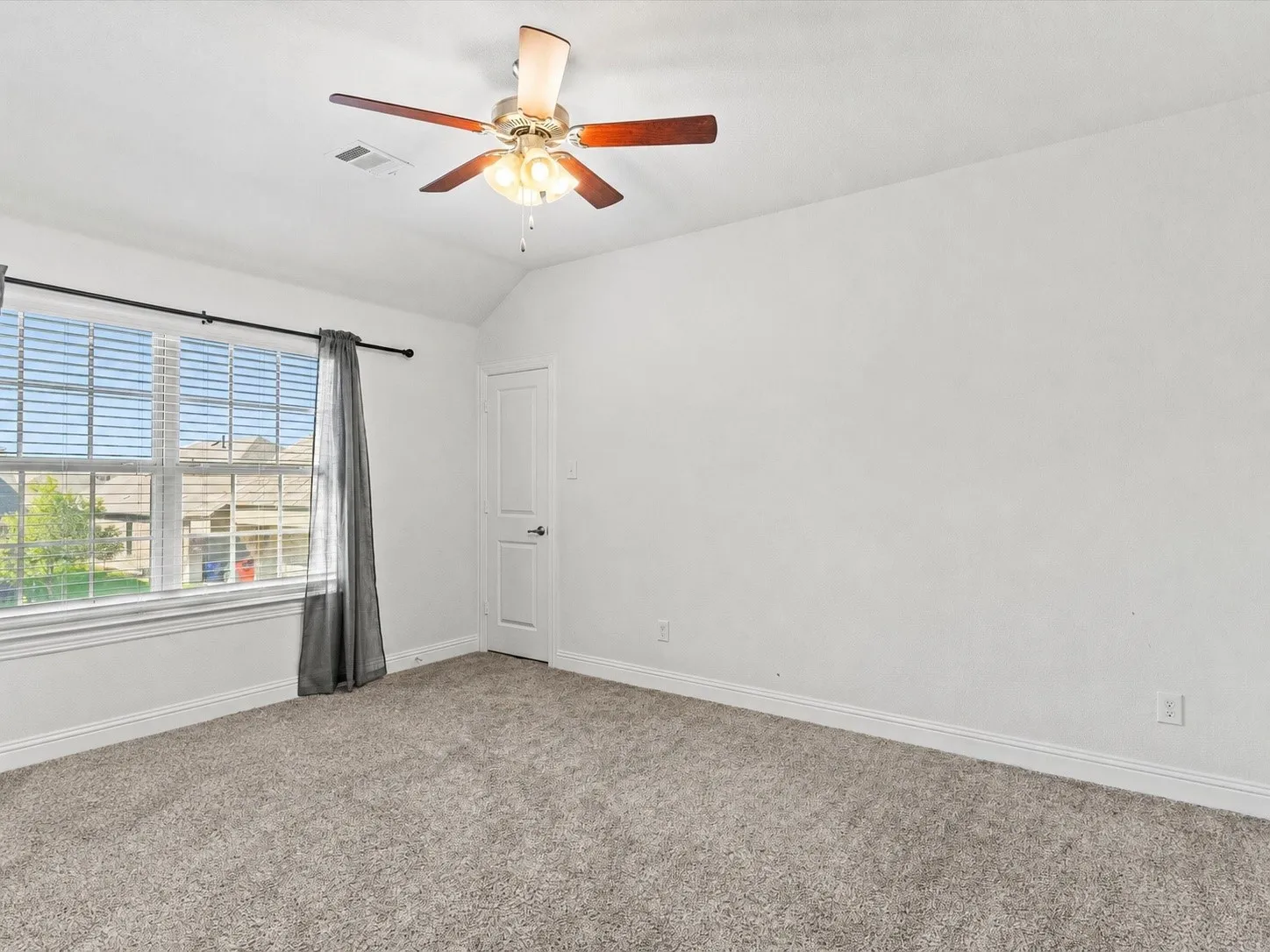 Carpeted room featuring a ceiling fan with light fixture, large window with blinds, and a white paneled door