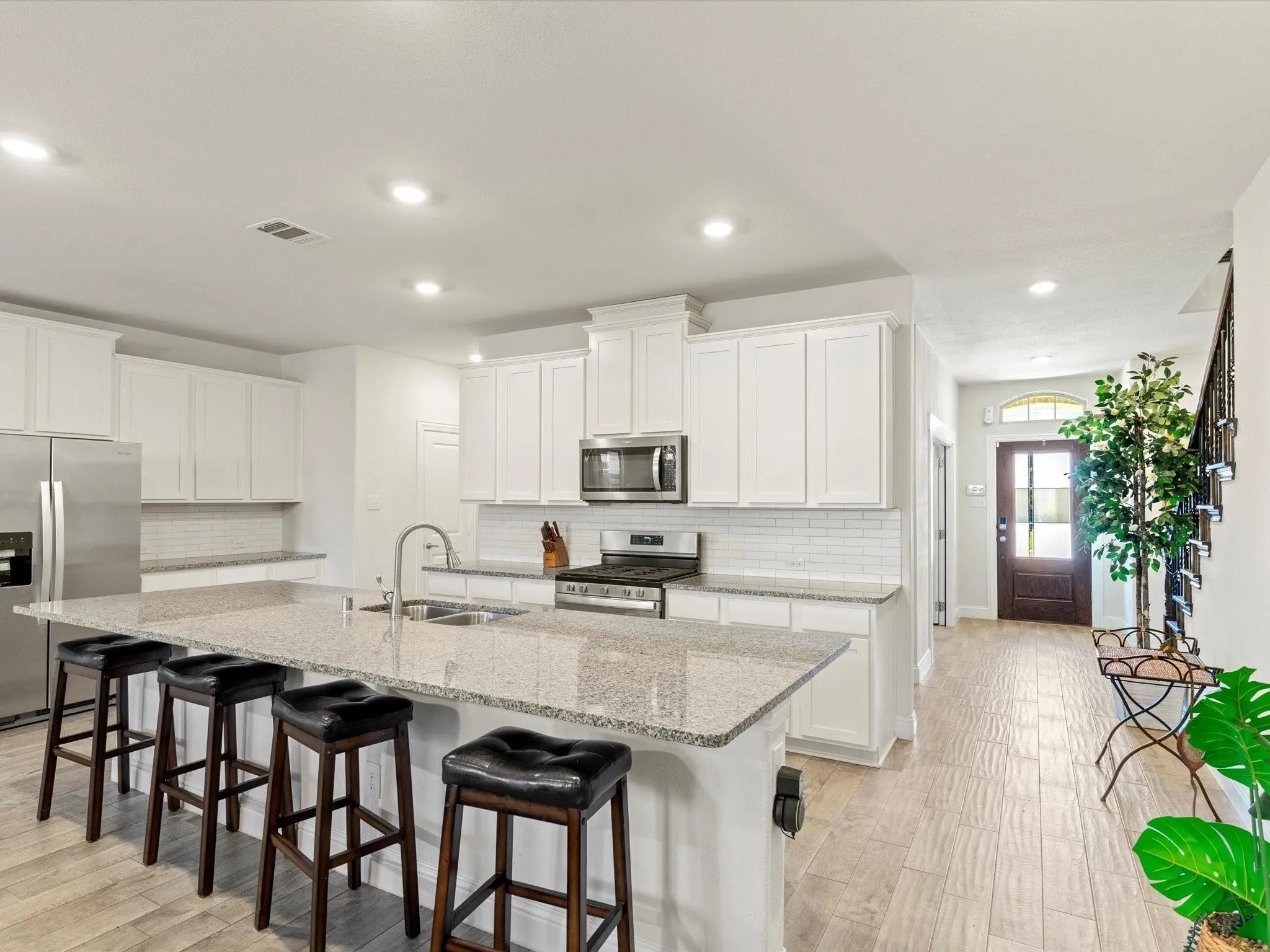 Kitchen featuring a large island with a double sink, stainless steel appliances, white cabinetry, and subway tile backsplash