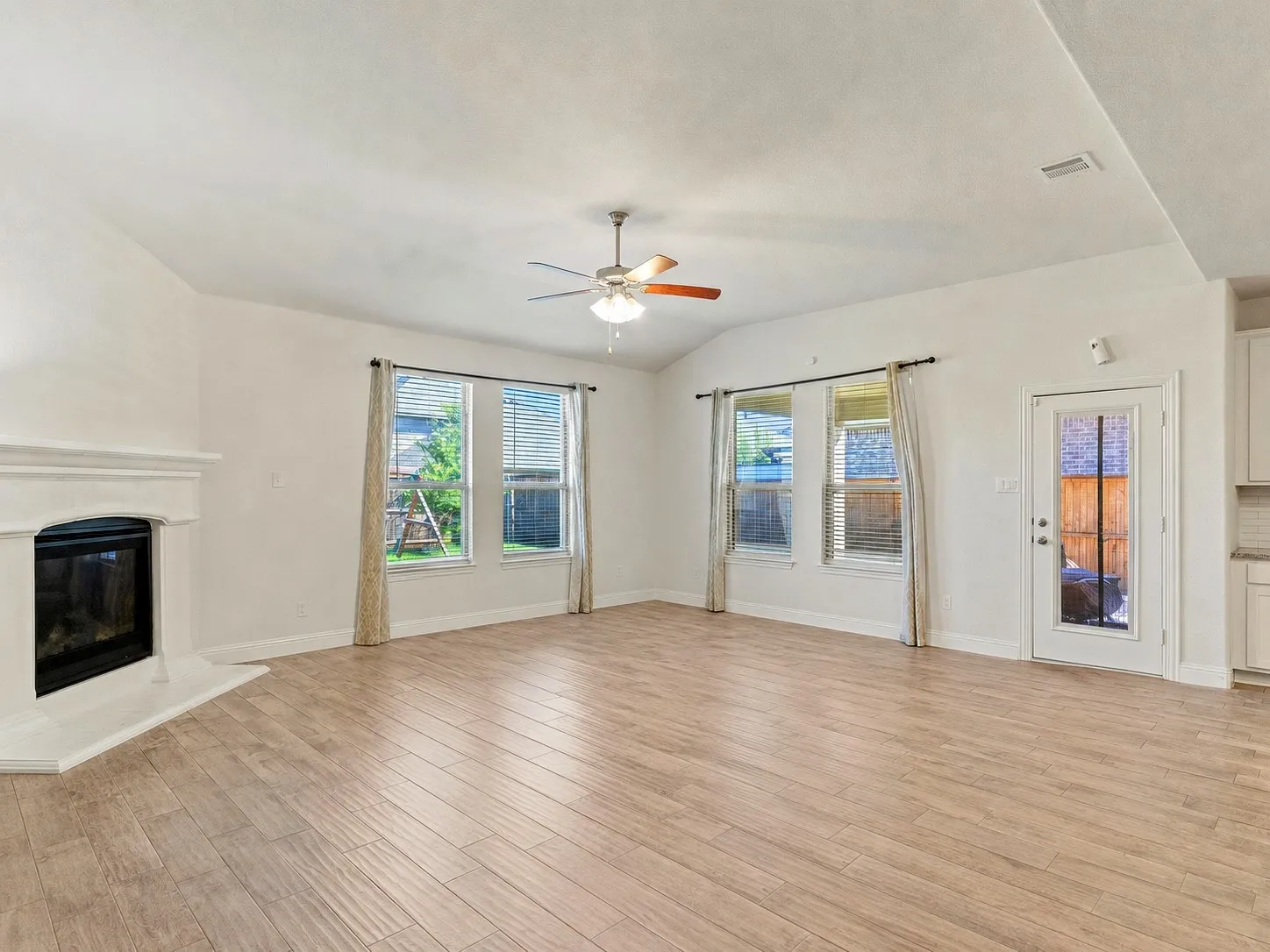 Spacious living area featuring wood-finish flooring, a corner fireplace with a white mantel, and two large windows