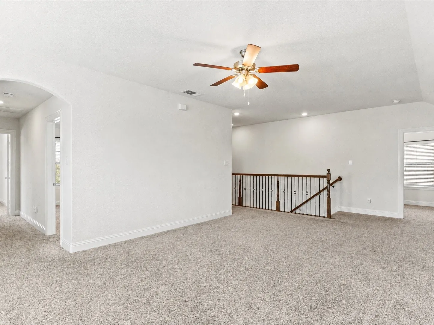 Expansive carpeted loft featuring a ceiling fan, recessed lighting, and a wrought iron and wood-finish railing