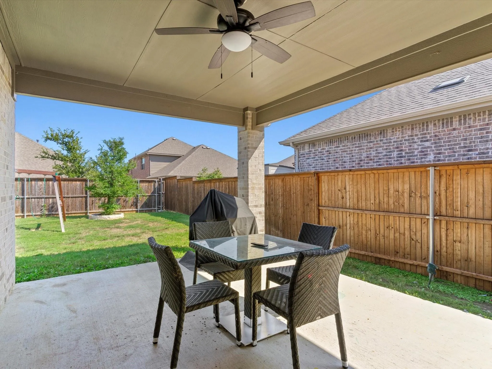 Covered patio with an integrated ceiling fan, concrete flooring, and brick support columns