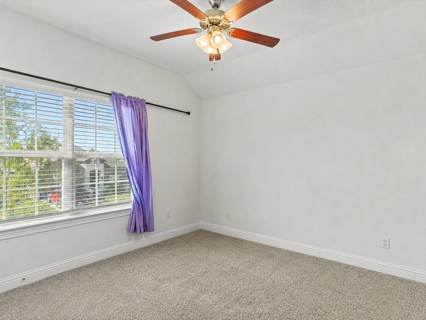 Carpeted room featuring a vaulted ceiling and a wood-finish ceiling fan with integrated lighting