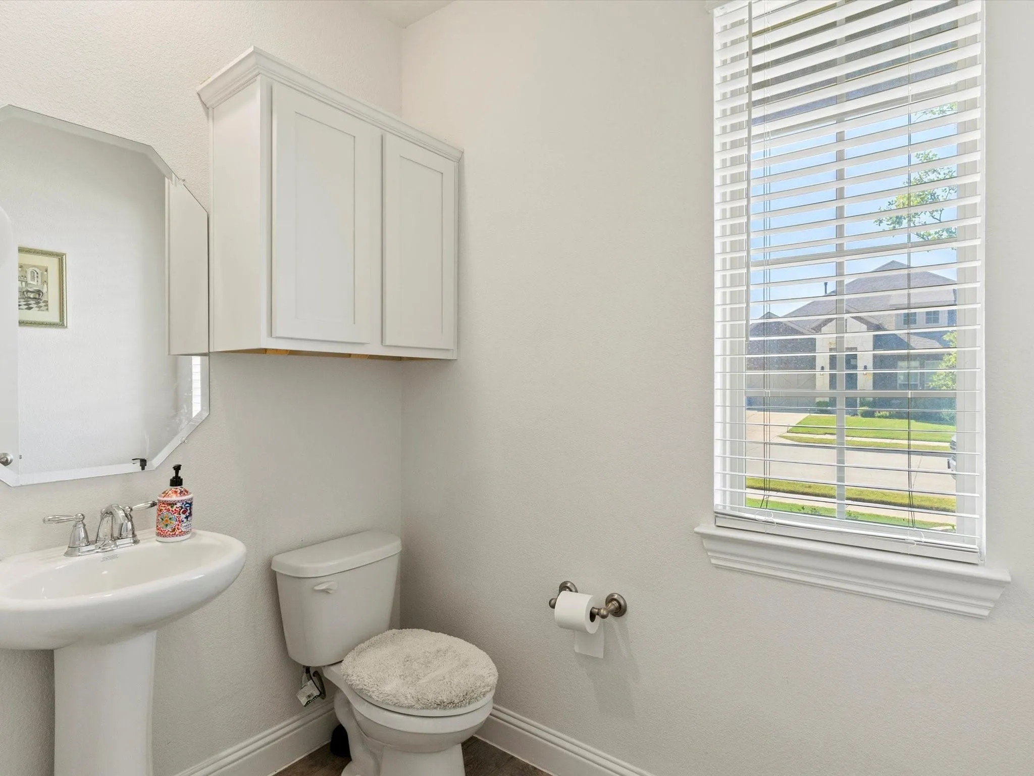 Well-appointed powder room featuring a pedestal sink with chrome faucet, octagonal wall mirror, and white shaker-style cabinetry with crown molding