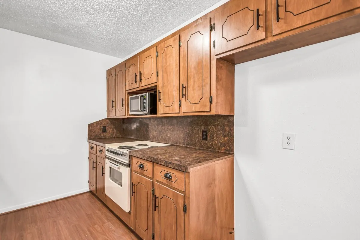 Kitchen featuring white electric stove, tasteful backsplash, dark countertops, and lot of cabinets for great storage.