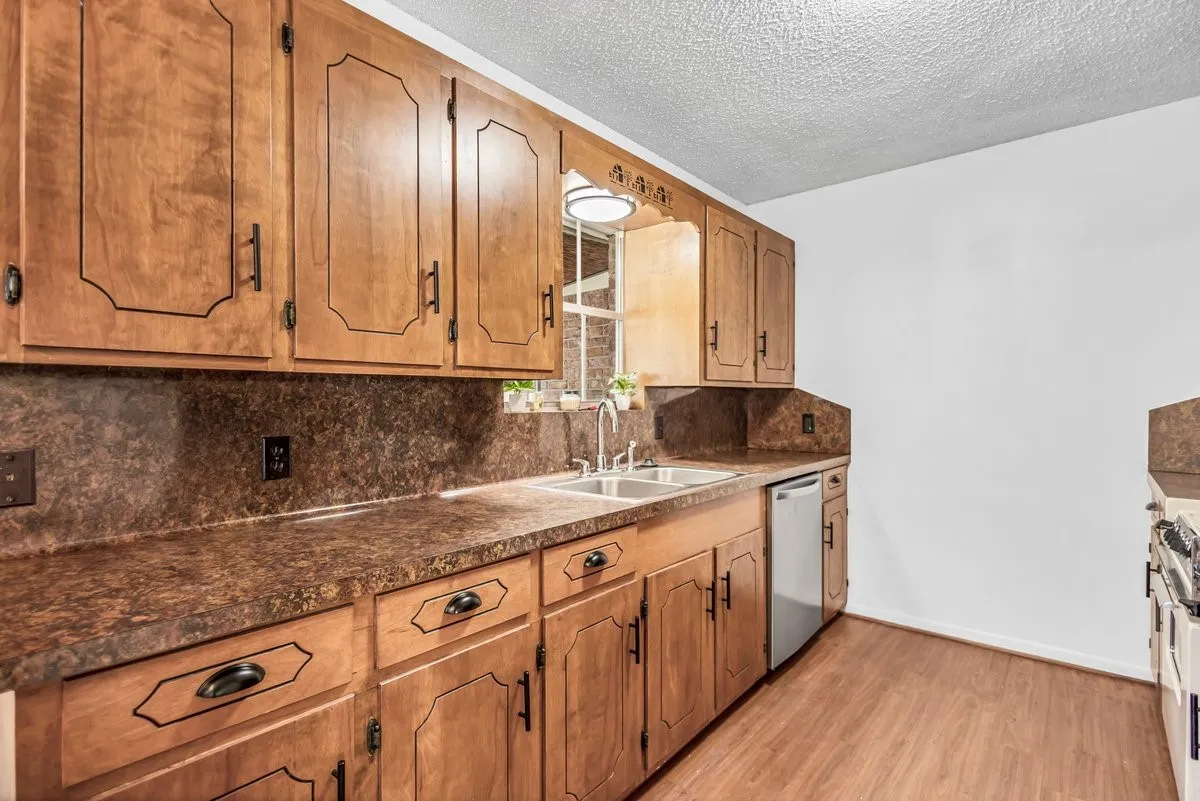Kitchen featuring backsplash, dark countertops, light wood finished floors, a textured ceiling, and updated dishwasher.