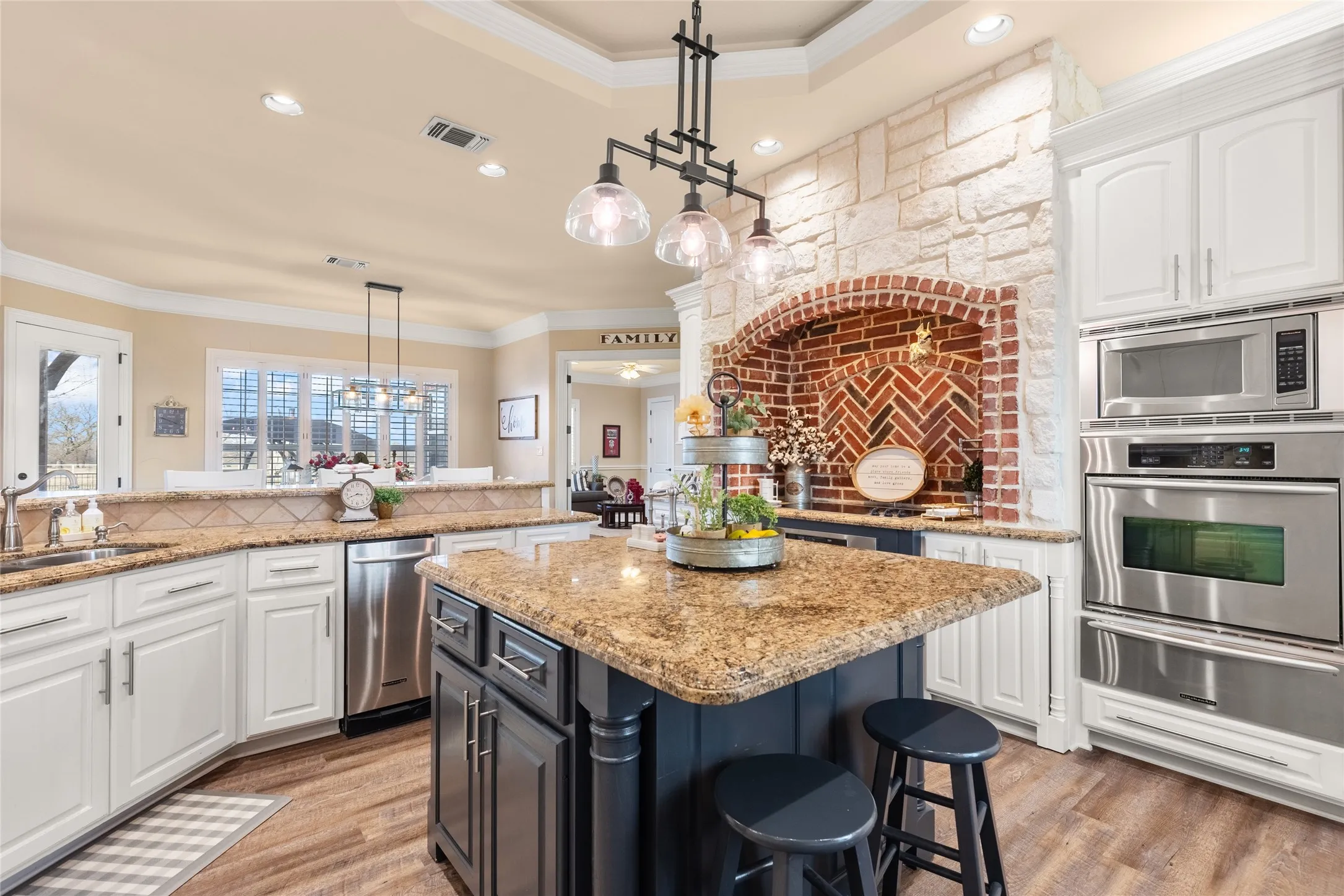 Two tone kitchen featuring ornamental molding, two tone color scheme, light stone counters, a warming drawer, and stainless steel appliances