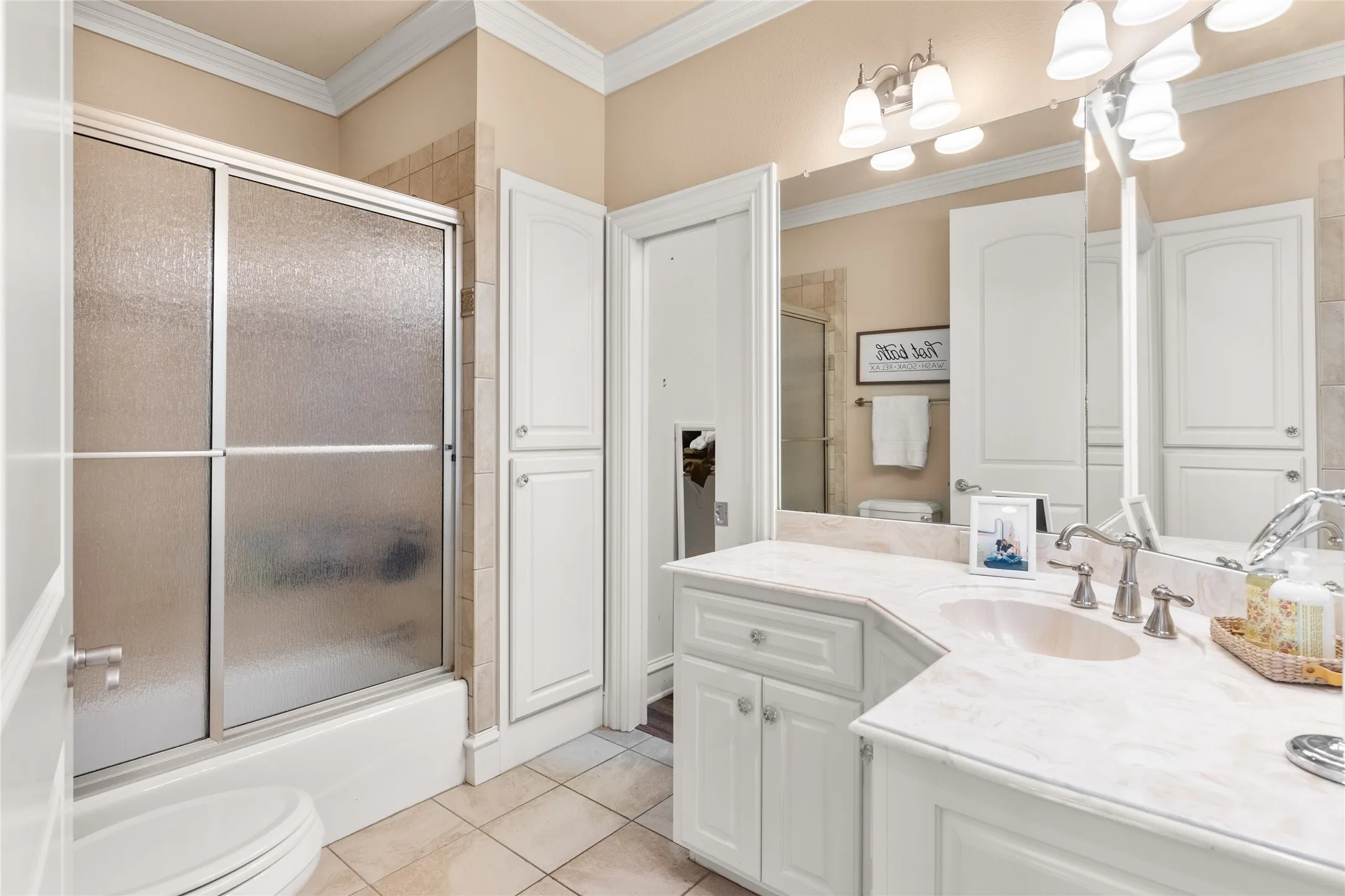 Bathroom with vanity, ornamental molding, enclosed tub / shower combo, and light tile patterned flooring