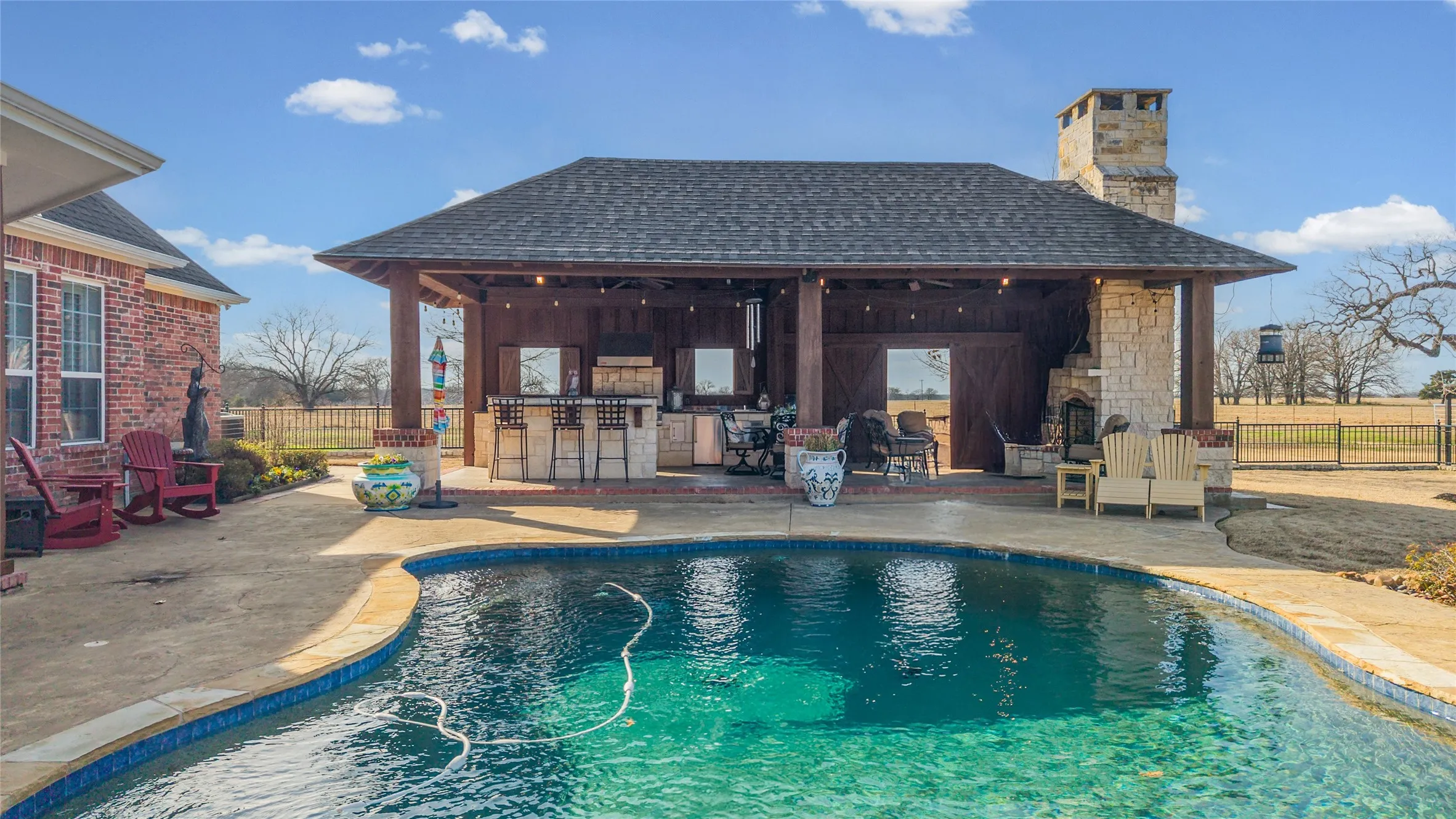 Back of house featuring an outdoor bar, a chimney, roof with shingles, a patio, and stone siding