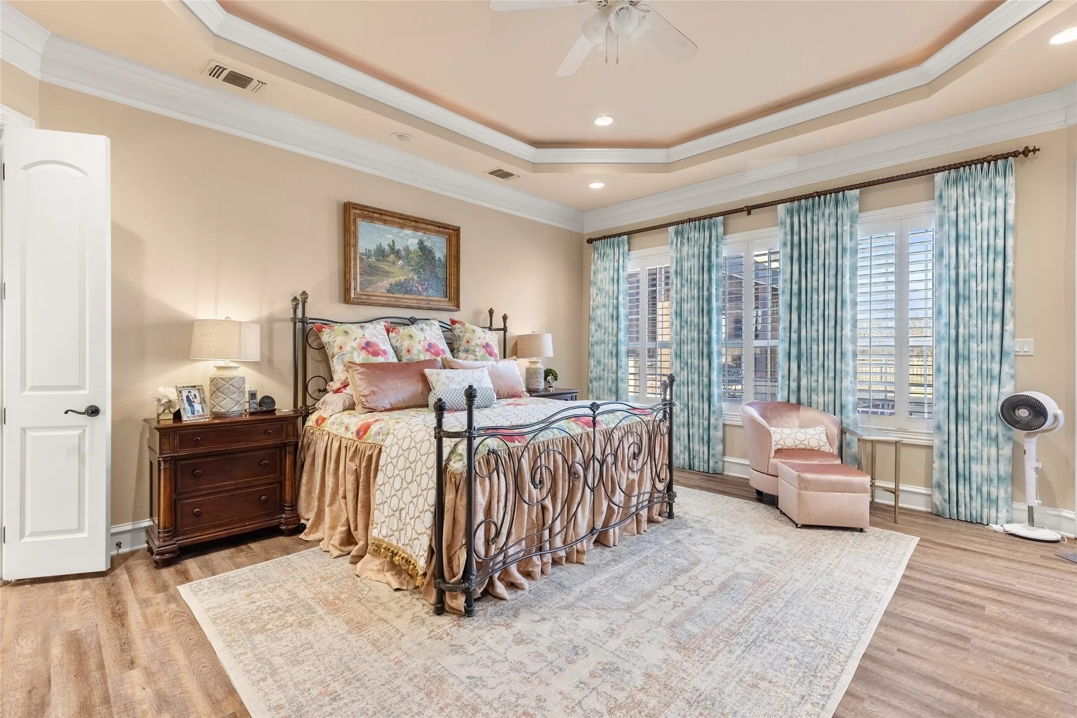 Bedroom with crown molding, light wood-style flooring, a ceiling fan, a tray ceiling, and recessed lighting