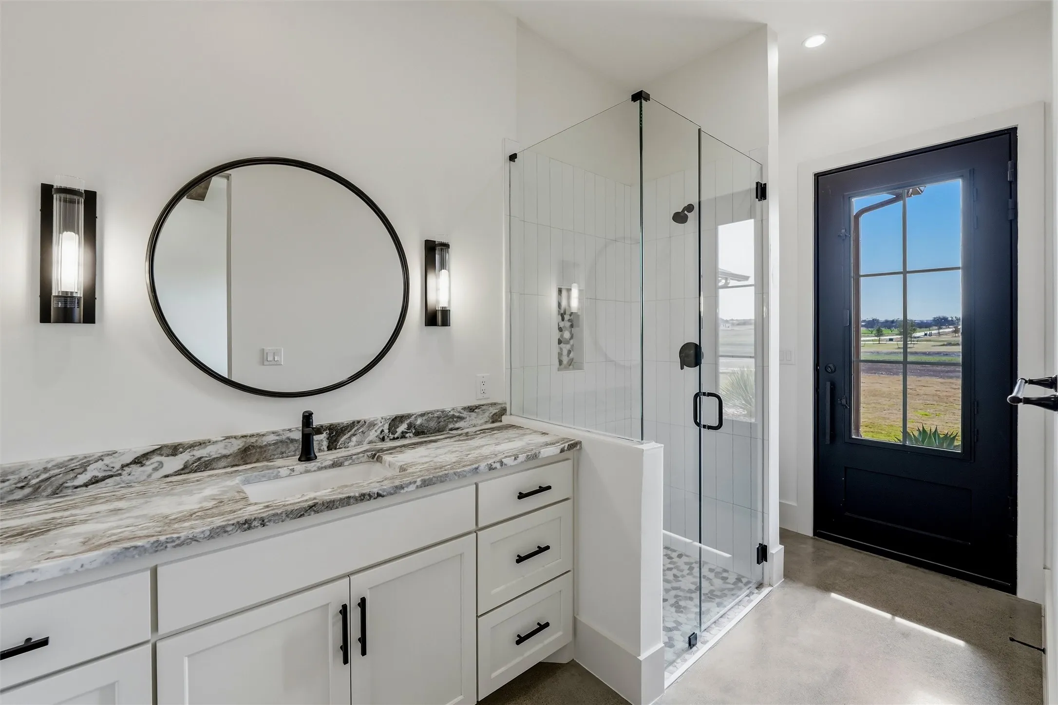 Bathroom featuring a shower stall, concrete flooring, vanity and door to outside