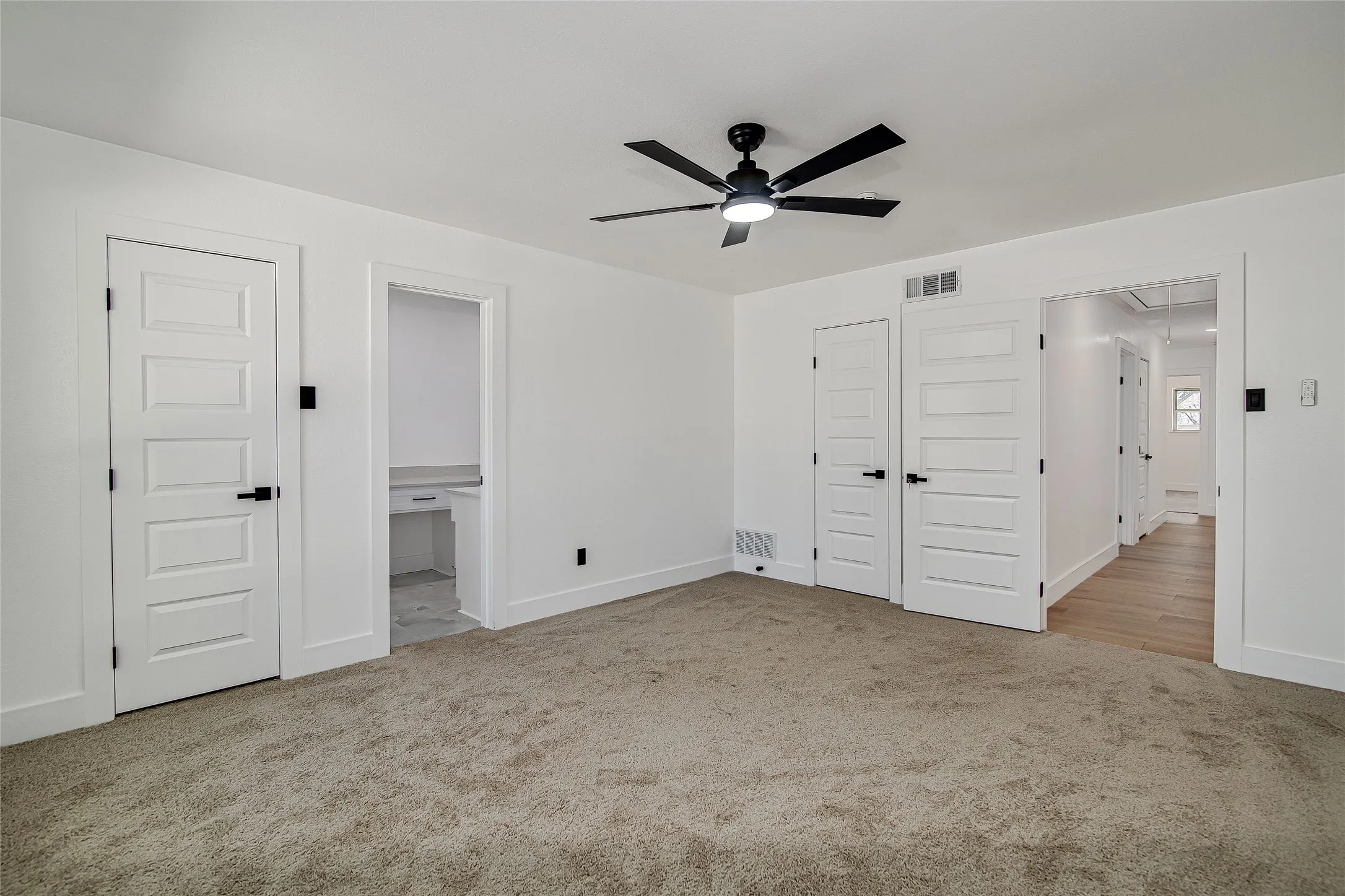Primary bedroom with light carpet, ensuite bath, a ceiling fan, and walk in closet