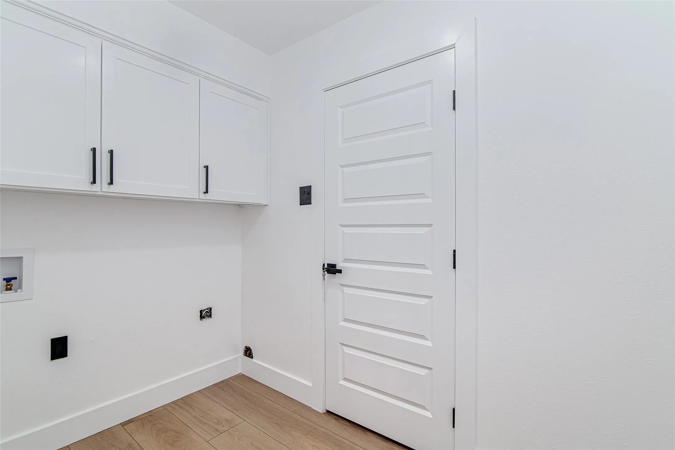 Laundry area with light wood-style flooring, washer hookup, and cabinet space