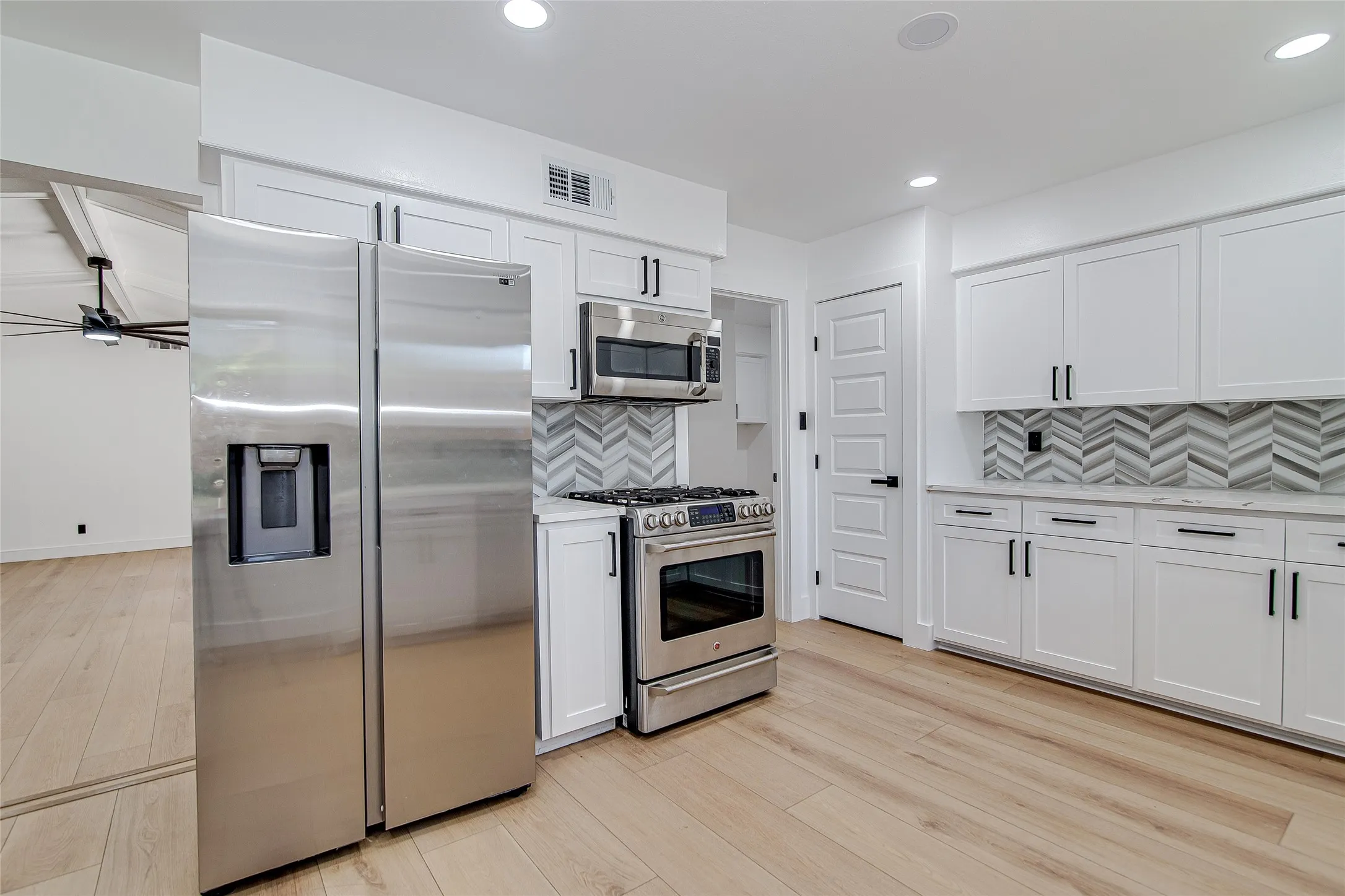 Kitchen with stainless steel appliances, light wood-type flooring, tasteful backsplash, white cabinetry, and recessed lighting