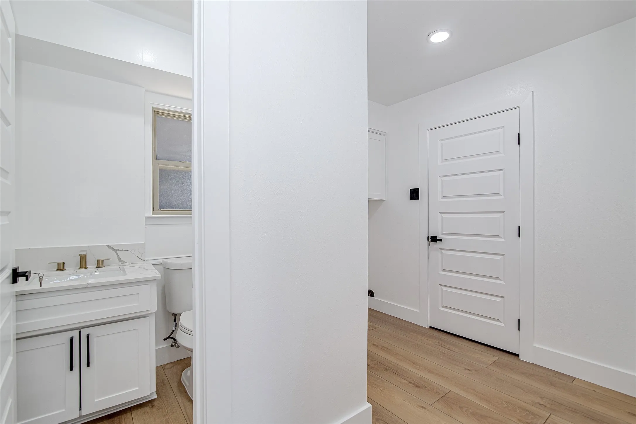 1/2 Bathroom featuring vanity, light wood-style floors, and recessed lighting leads into the laundry room and the door to exit into the garage.