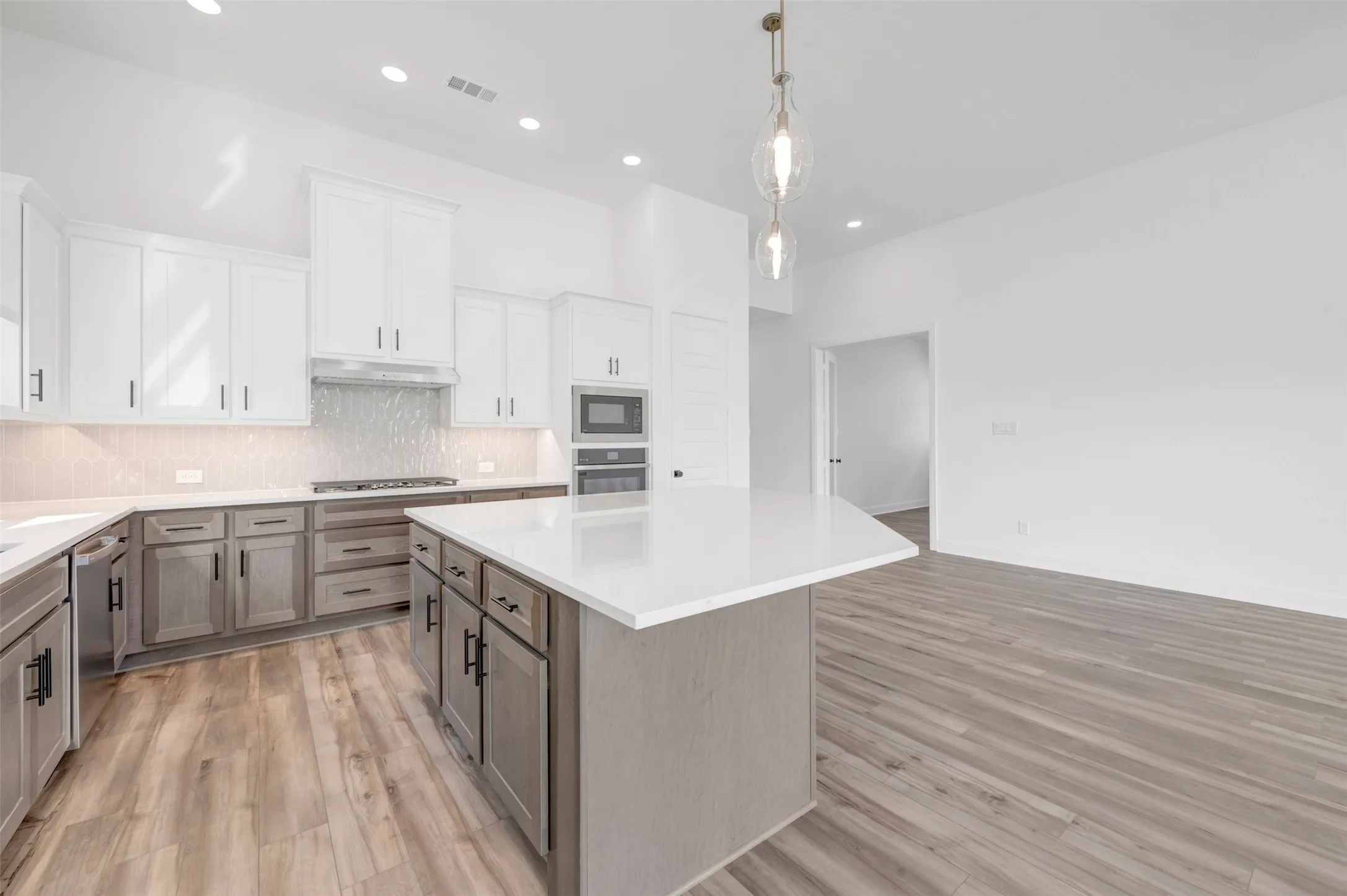 Contemporary kitchen featuring a large central island with a solid surface countertop, two-tone cabinetry, stainless steel appliances, a tiled backsplash, and recessed lighting