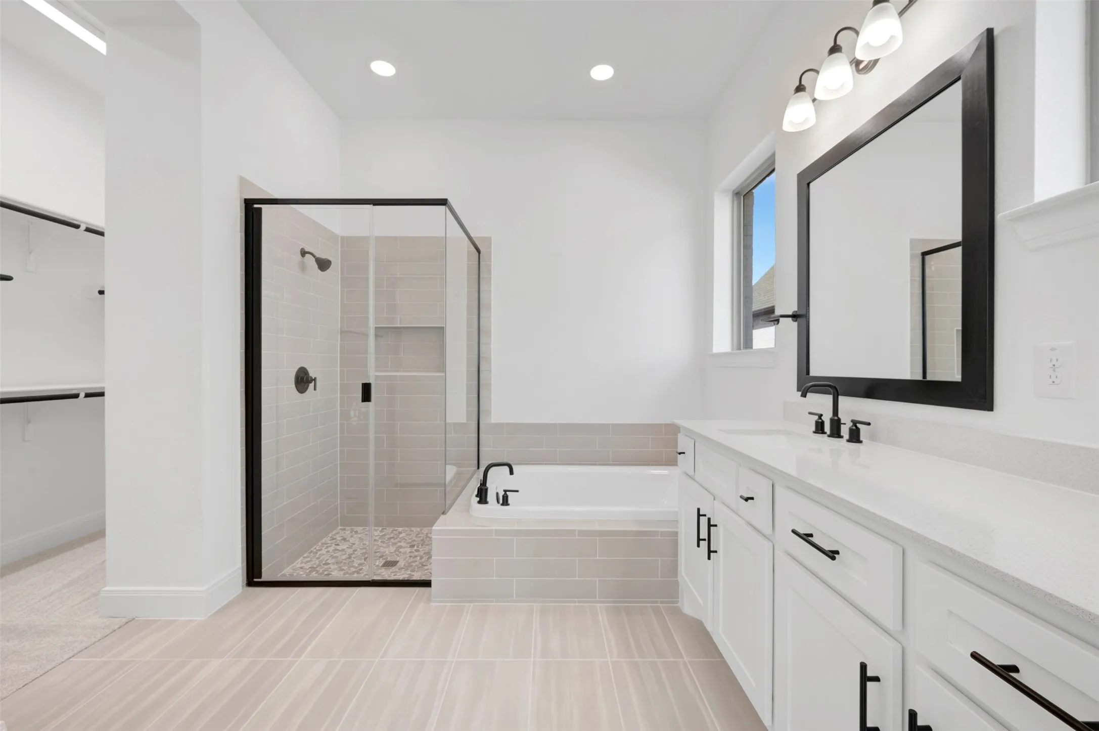 Modern bathroom featuring a soaking tub, glass-enclosed shower with tiled walls and pebble flooring, a wide vanity with white cabinetry, a single sink, and matte black hardware