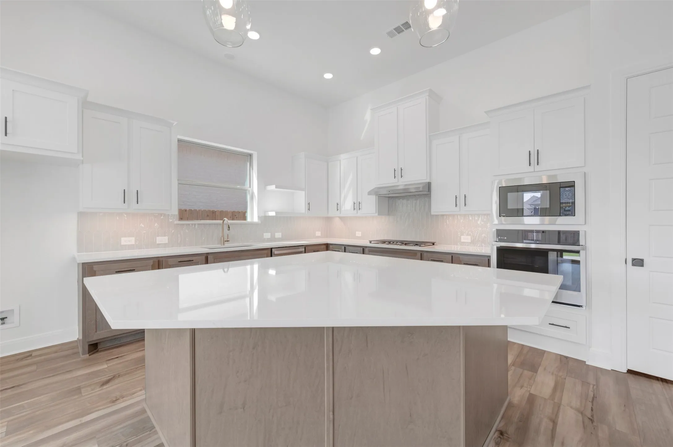 Spacious kitchen featuring a large central island with a light-toned countertop, white upper cabinetry, and contrasting darker base cabinetry