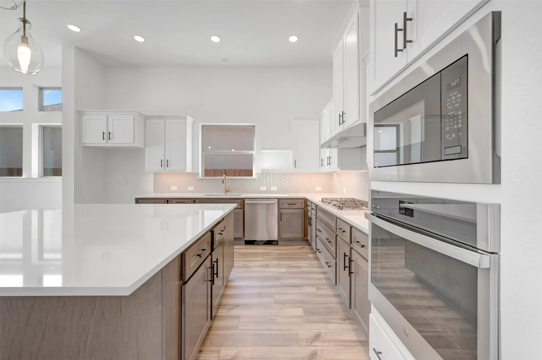 Spacious kitchen featuring a large central island with light-toned countertops, white upper cabinetry, wood-finish lower cabinetry, stainless steel appliances, and wood-finish flooring