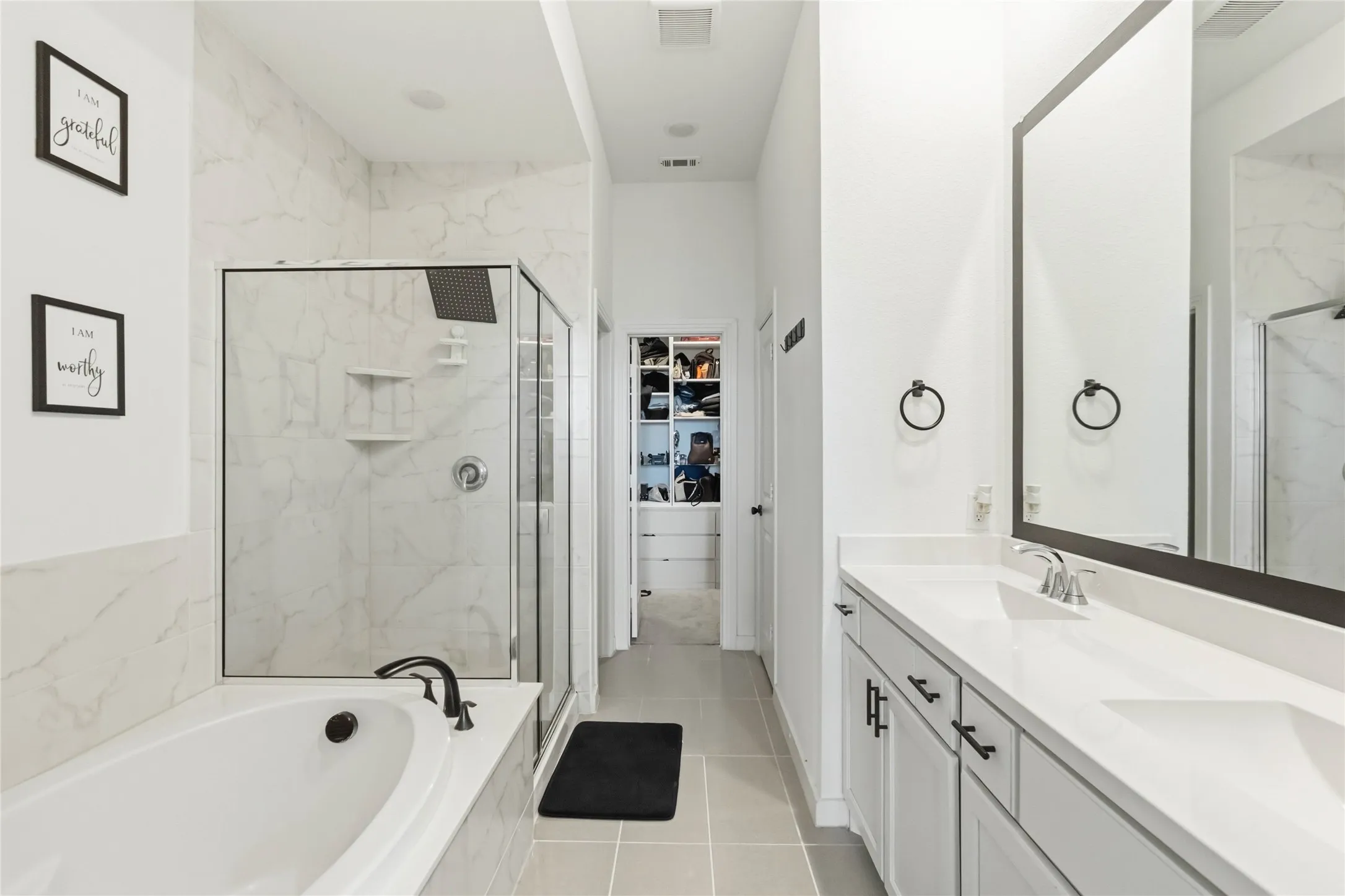 Full bath featuring double vanity, a spacious closet, a marble finish shower, a bath, and light tile patterned floors