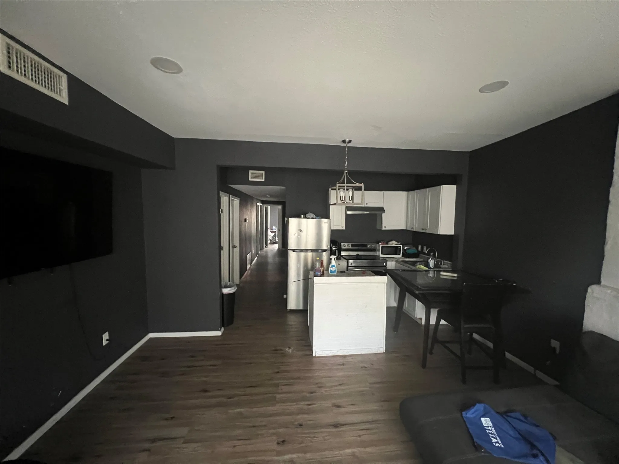 Kitchen with white cabinetry, decorative light fixtures, stainless steel appliances, dark wood finished floors, and open floor plan