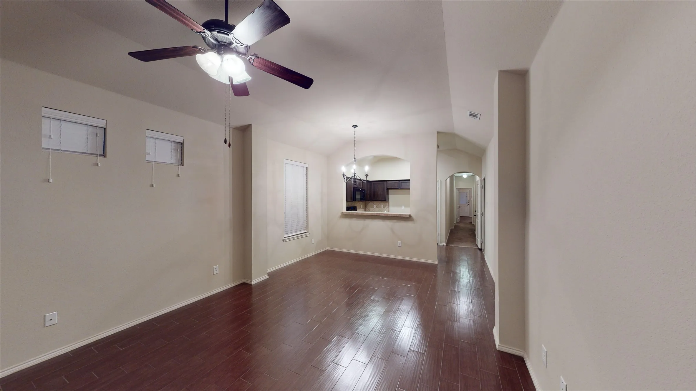 Unfurnished living room featuring a ceiling fan, a chandelier, dark wood-style floors, vaulted ceiling, and arched walkways