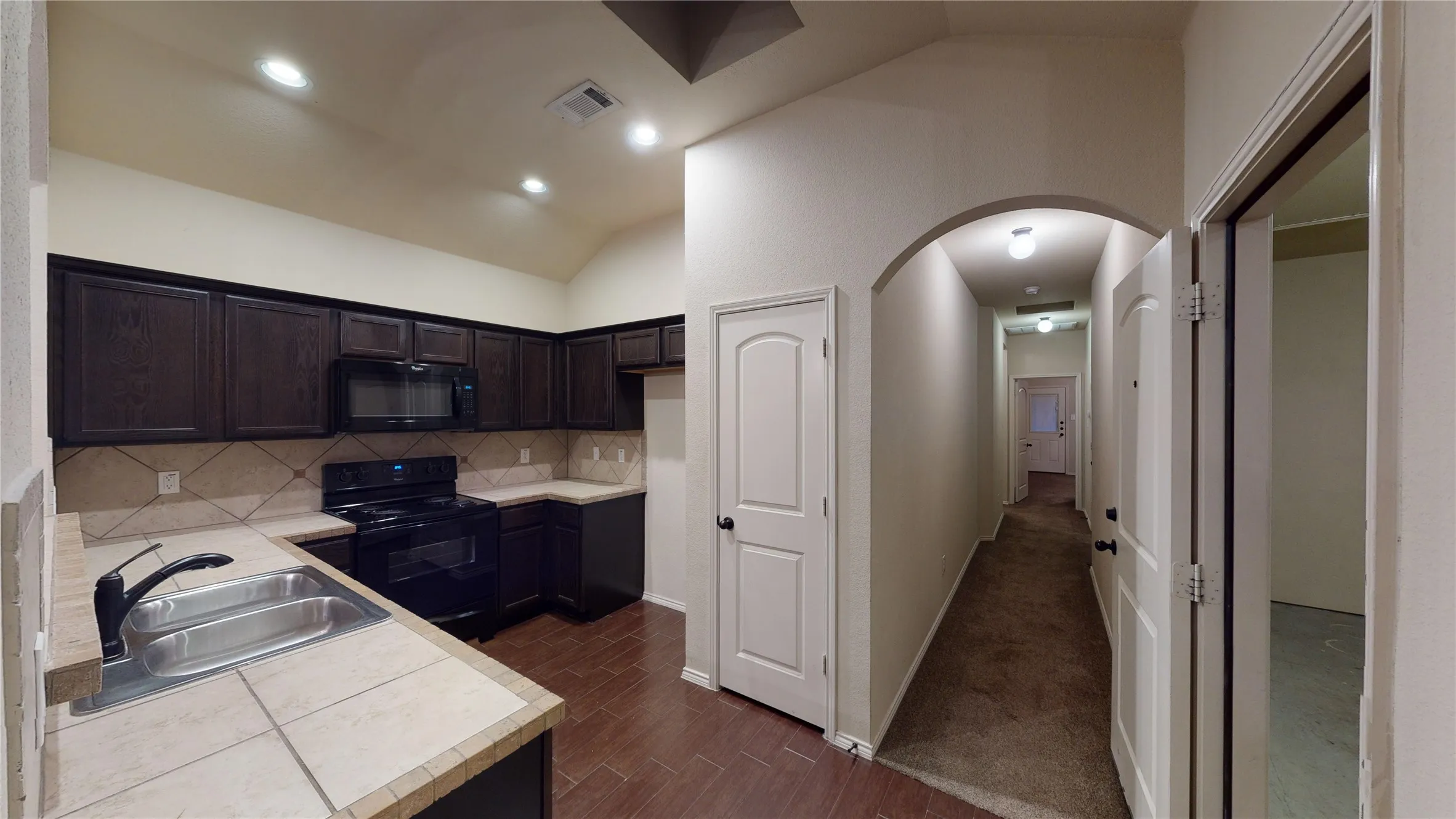Kitchen featuring black appliances, arched walkways, vaulted ceiling, tasteful backsplash, and wood tiled floors