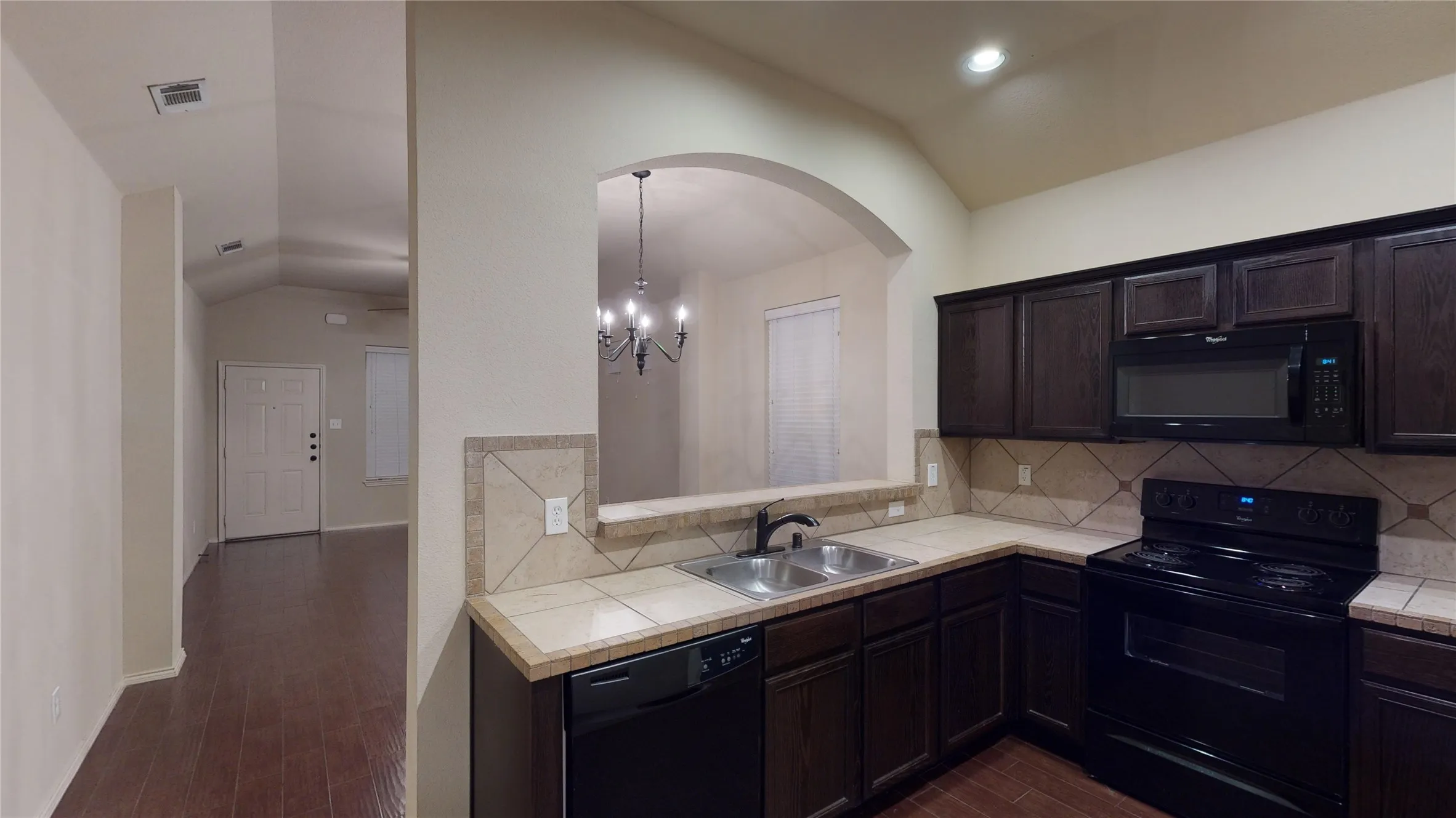 Kitchen with black appliances, tile countertops, lofted ceiling, decorative backsplash, and dark wood finished floors