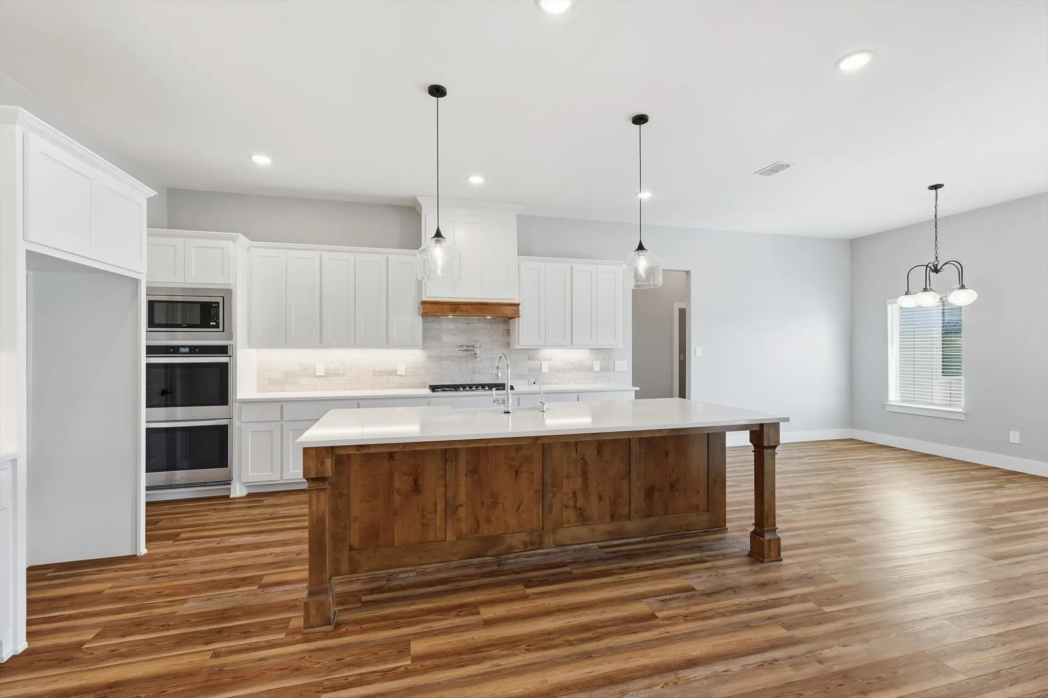 A showpiece kitchen built for gathering. Oversized island with warm wood base, quartz counters, bright white cabinetry, and modern pendant lighting—clean, open, and ready to host.