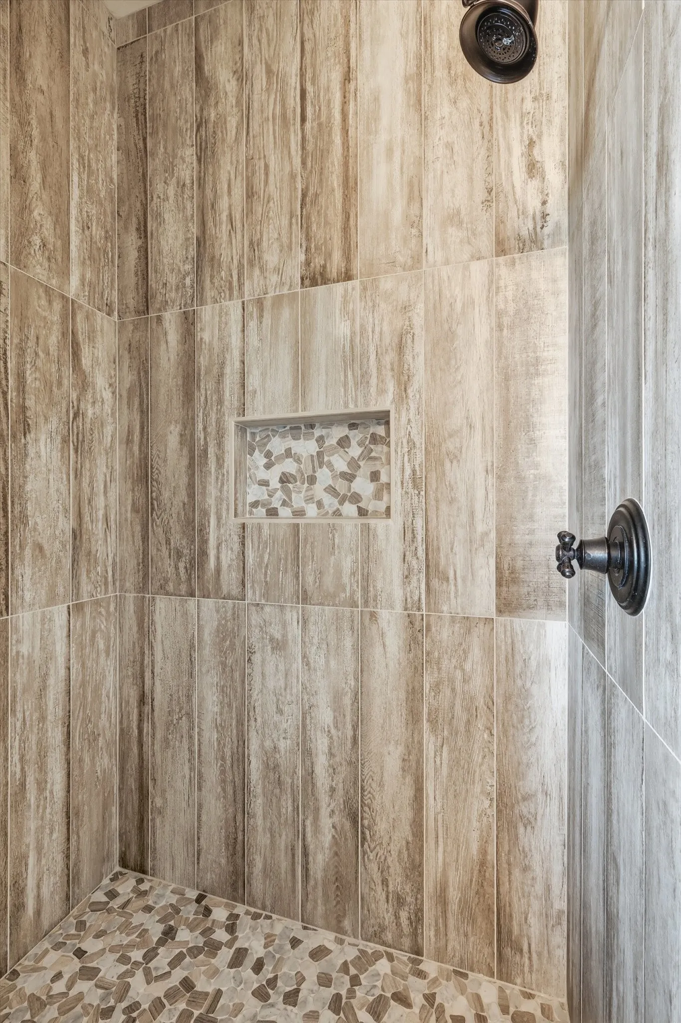 Custom walk-in shower. Beautiful tile work, niche detail, and pebble-style floor—built to feel like a high-end retreat.