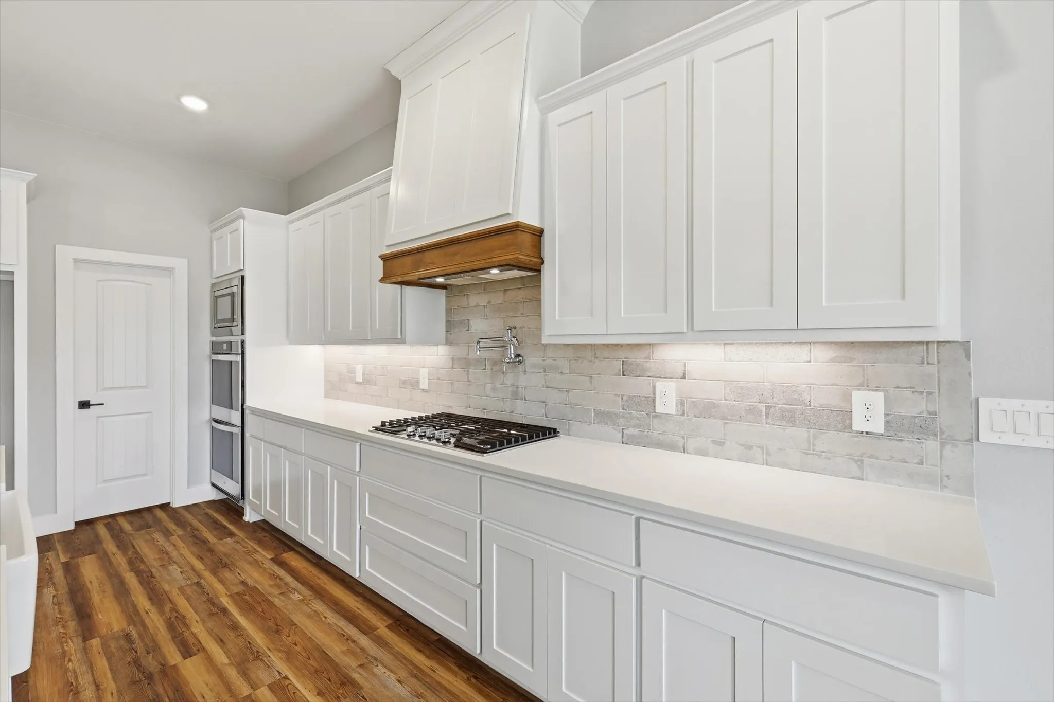 Serious cooking space. Long stretches of counter, a gas cooktop, designer vent hood, and a bright subway-tile backsplash—clean and elevated farmhouse style.