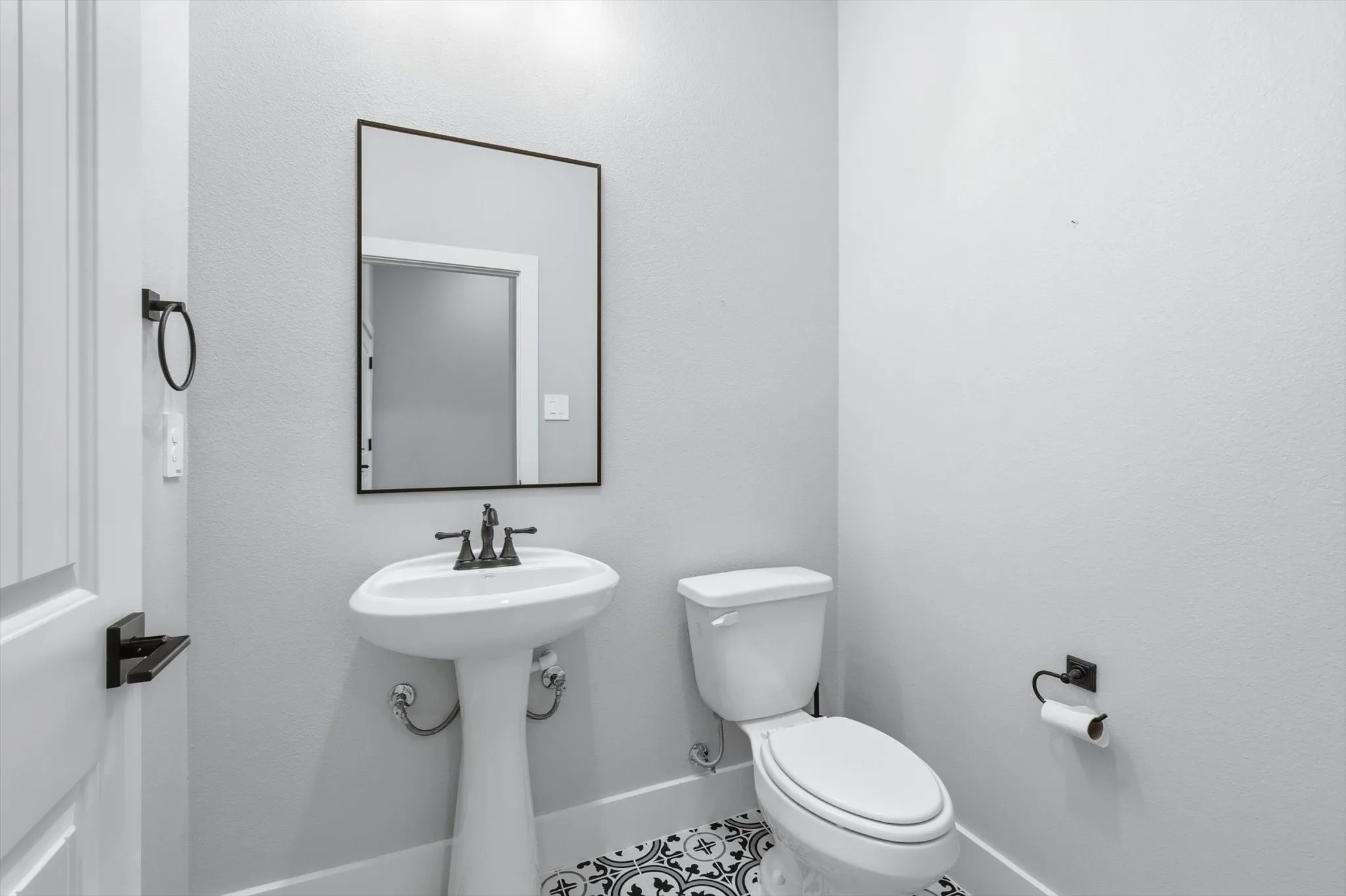 Designer powder bath. Pedestal sink, matte black hardware, and bold patterned tile that adds personality without overdoing it.