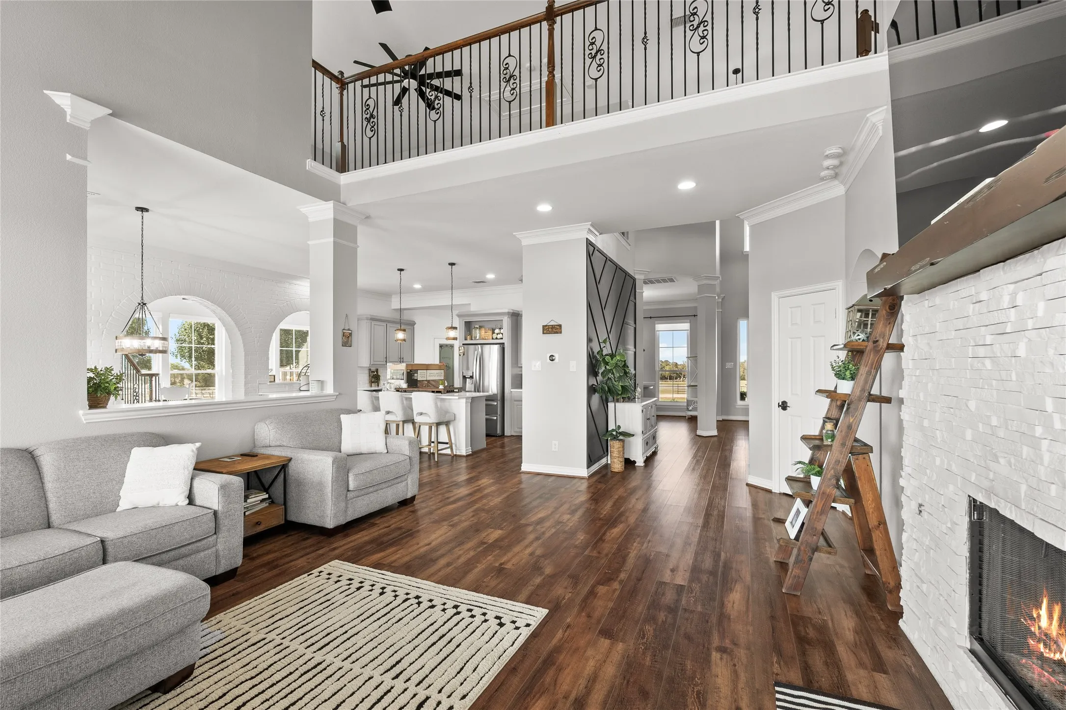 Living area featuring a lit fireplace, dark wood-type flooring, crown molding, a towering ceiling, and ceiling fan