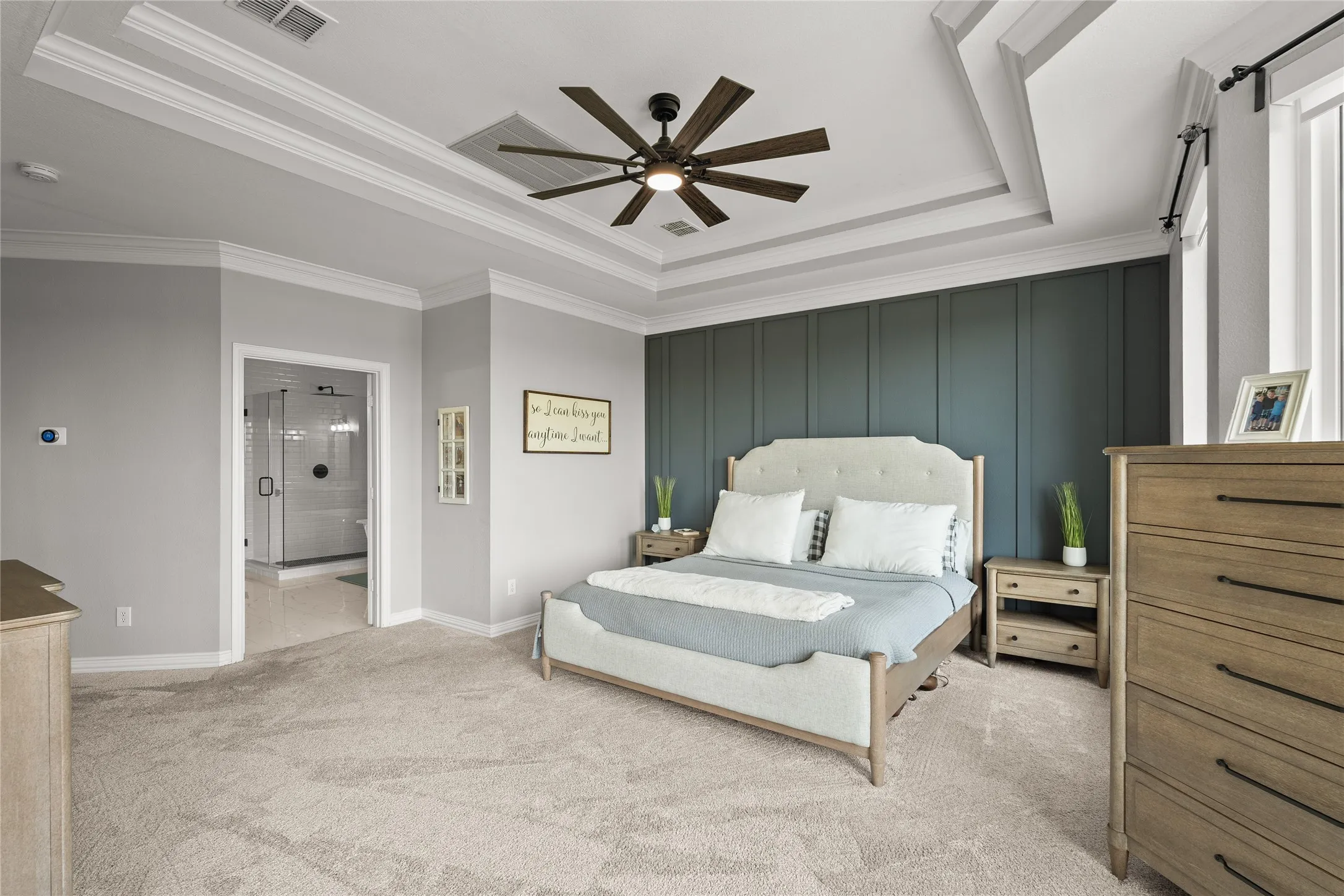 Bedroom featuring a tray ceiling, carpet floors, a decorative wall, a ceiling fan, and crown molding