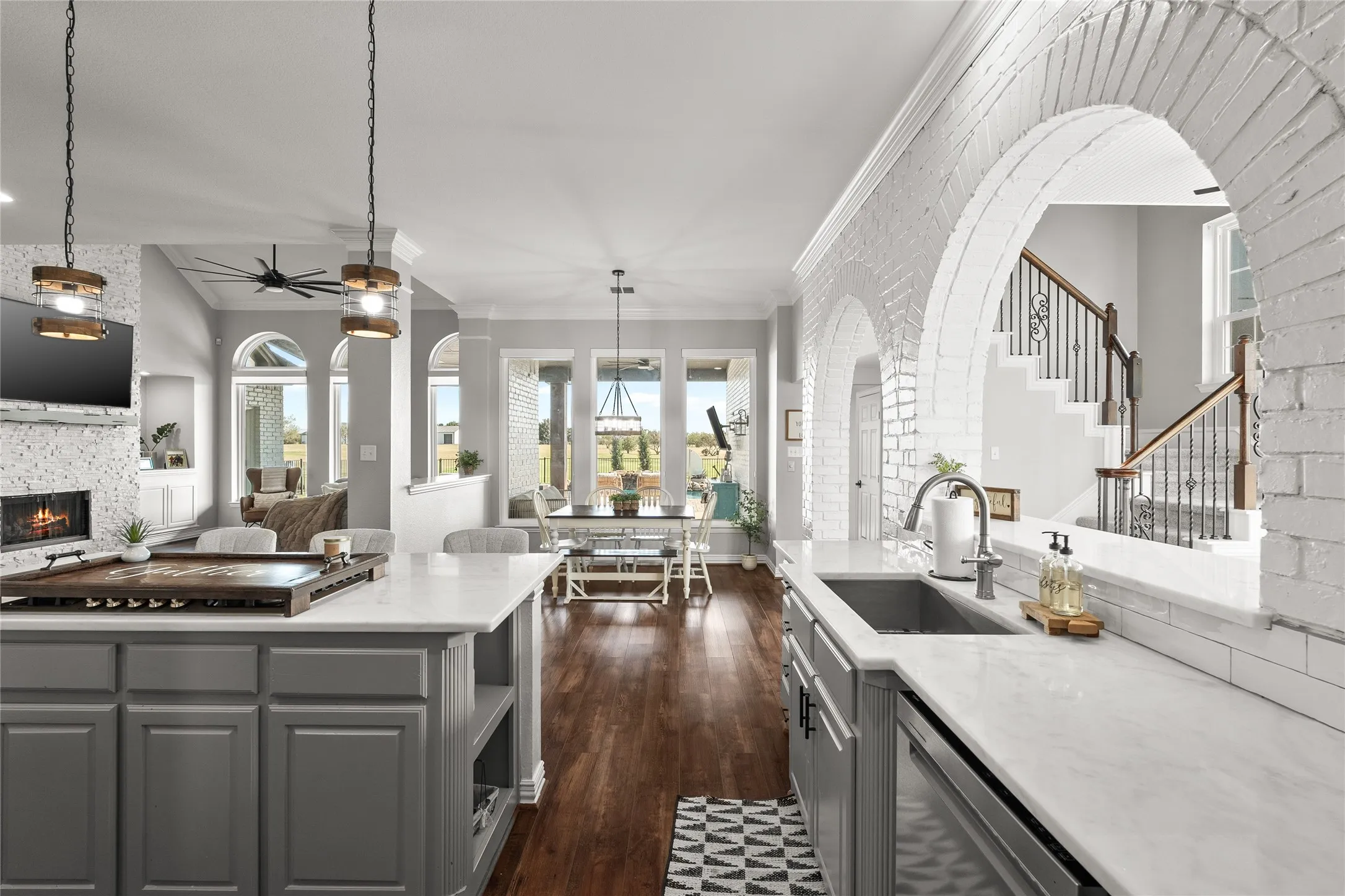 Kitchen with gray cabinets, hanging light fixtures, a large fireplace, dark wood-style flooring, and open floor plan
