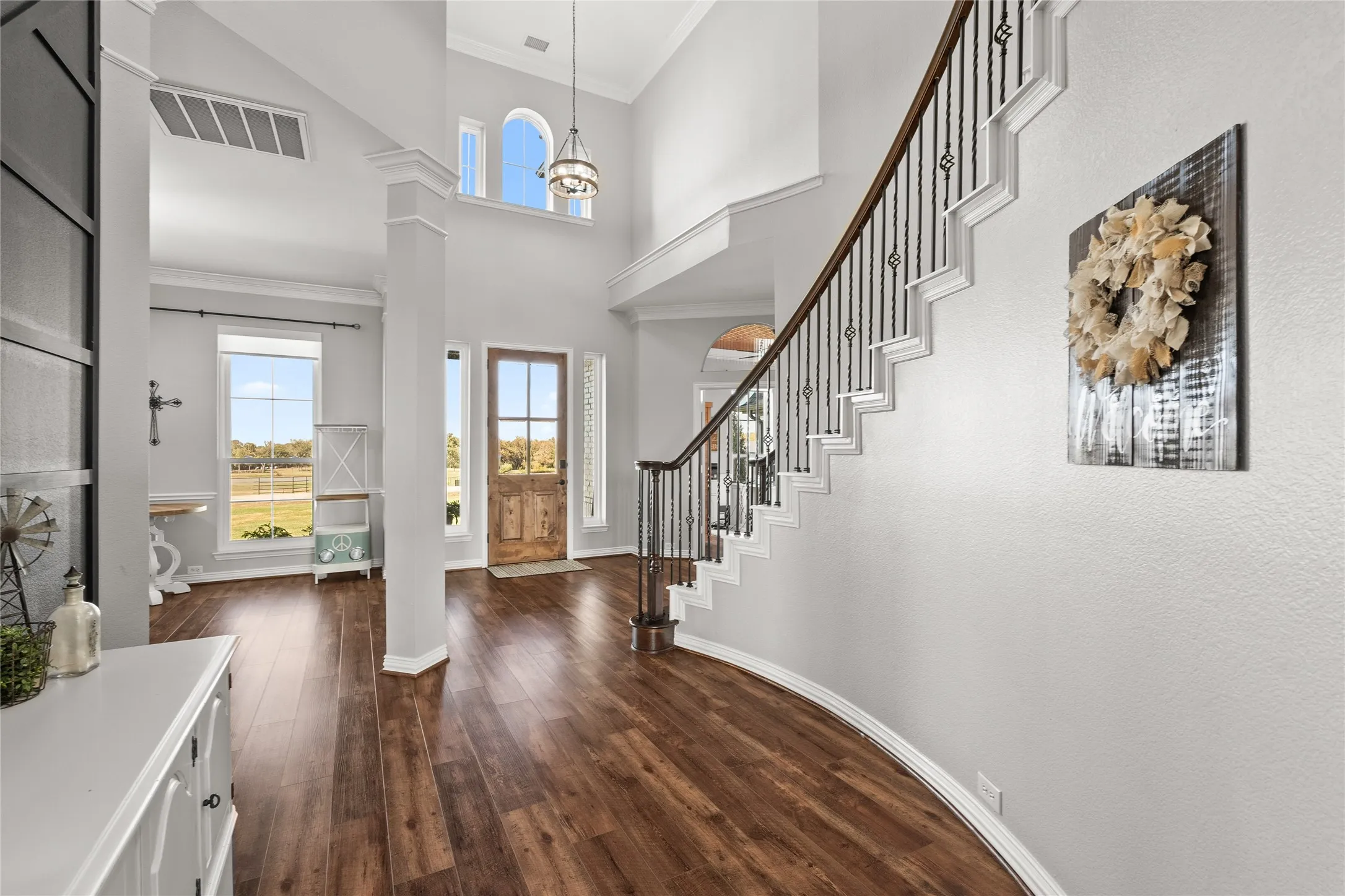 Foyer with a towering ceiling, ornamental molding, dark wood-type flooring, stairs, and arched walkways
