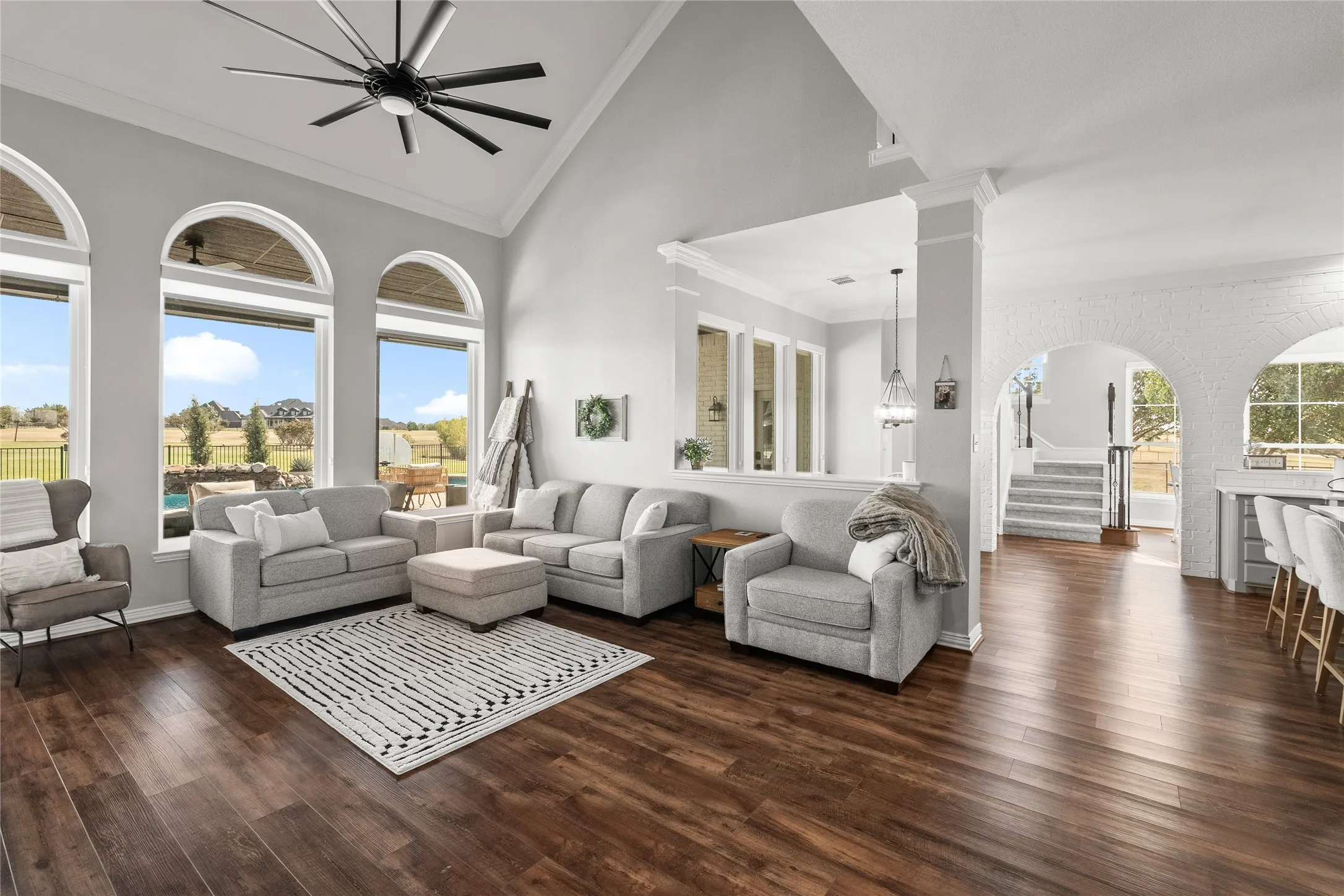 Living area featuring high vaulted ceiling, stairs, dark wood finished floors, ornamental molding, and ceiling fan