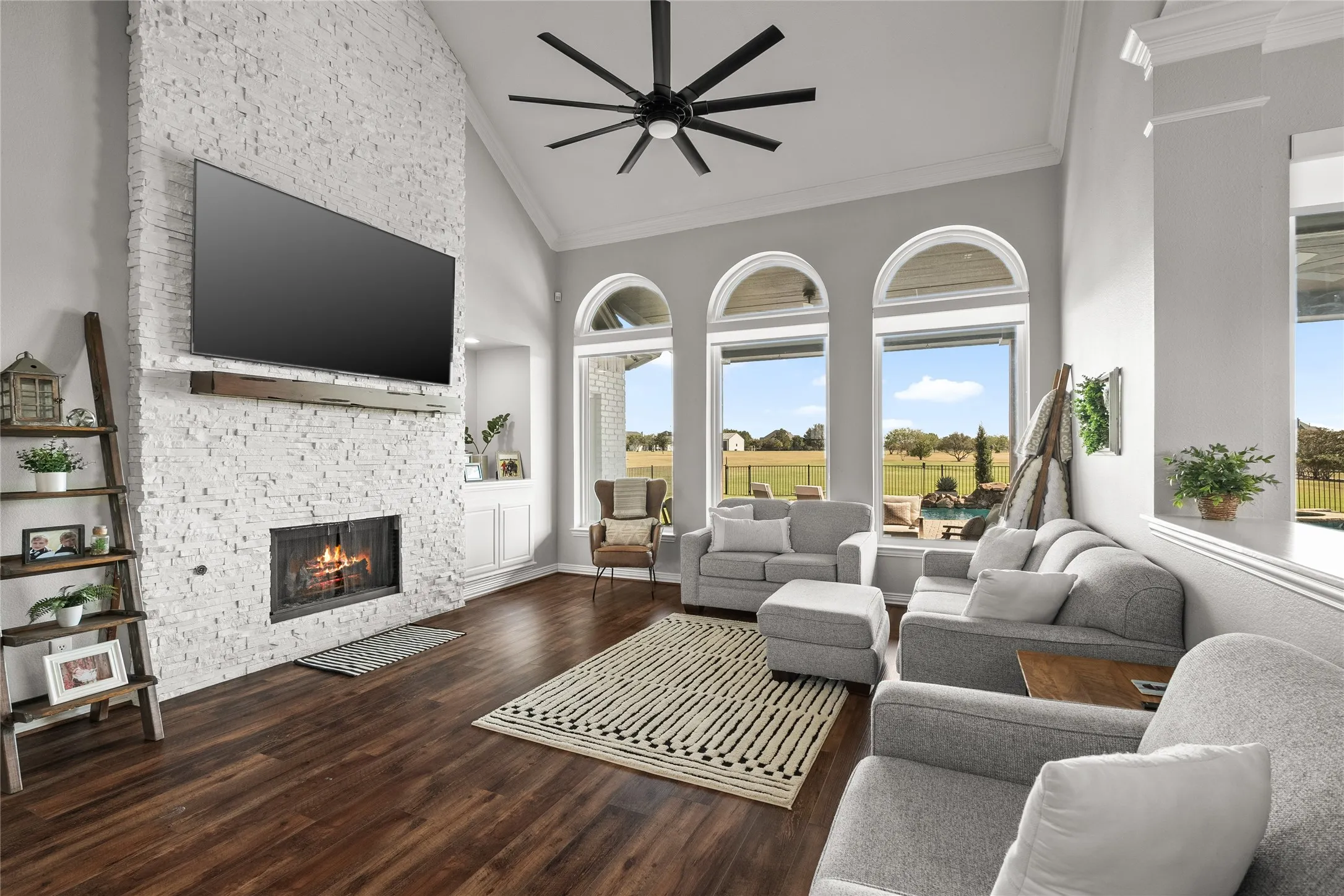 Living room featuring high vaulted ceiling, a fireplace, dark wood-style floors, a ceiling fan, and ornamental molding
