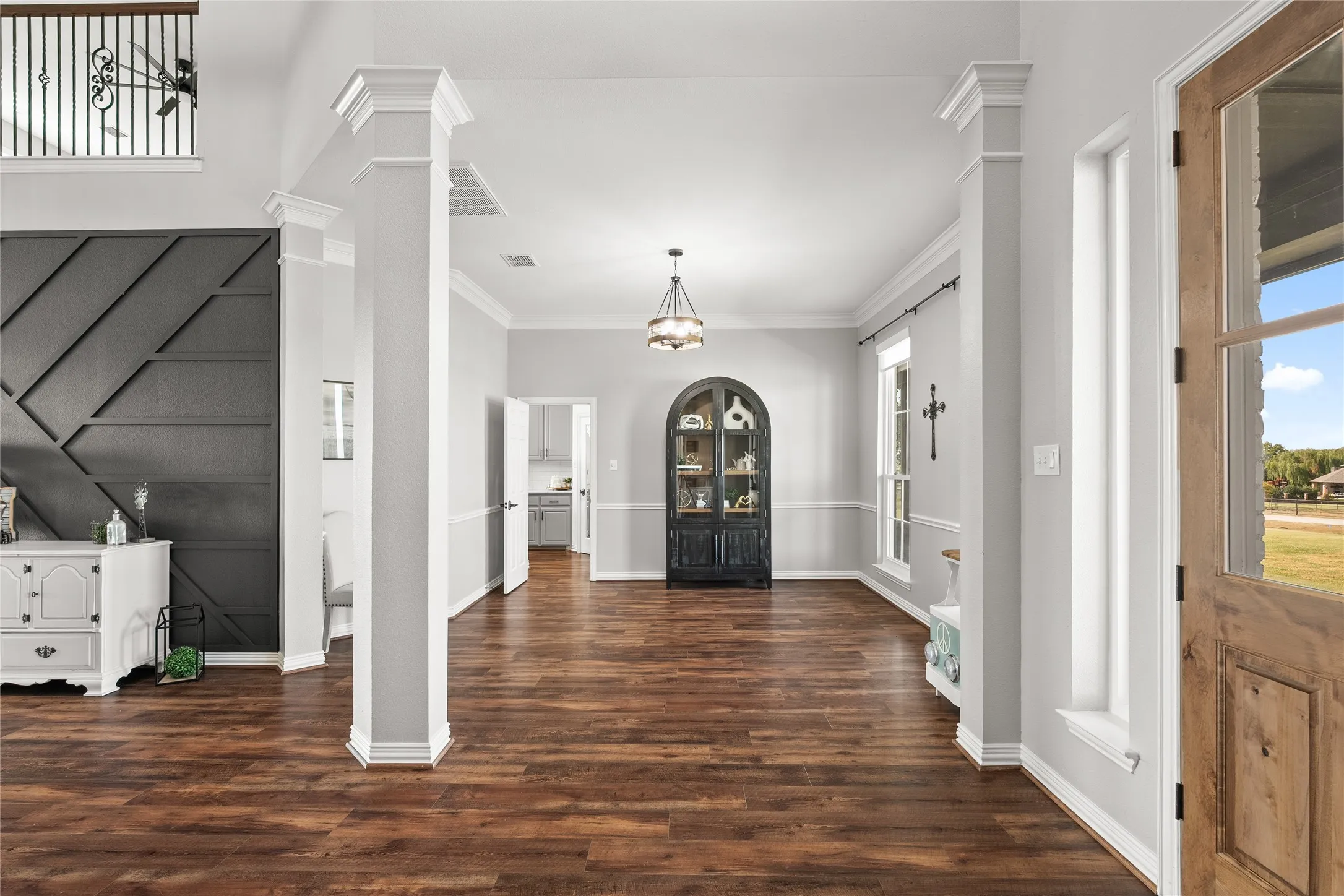 Entrance foyer featuring dark wood-style floors, ornamental molding, and decorative columns