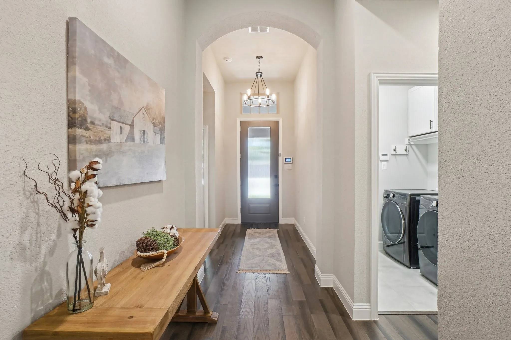 Foyer entrance with a chandelier, dark wood finished floors, arched walkways, washer and dryer, and a textured wall