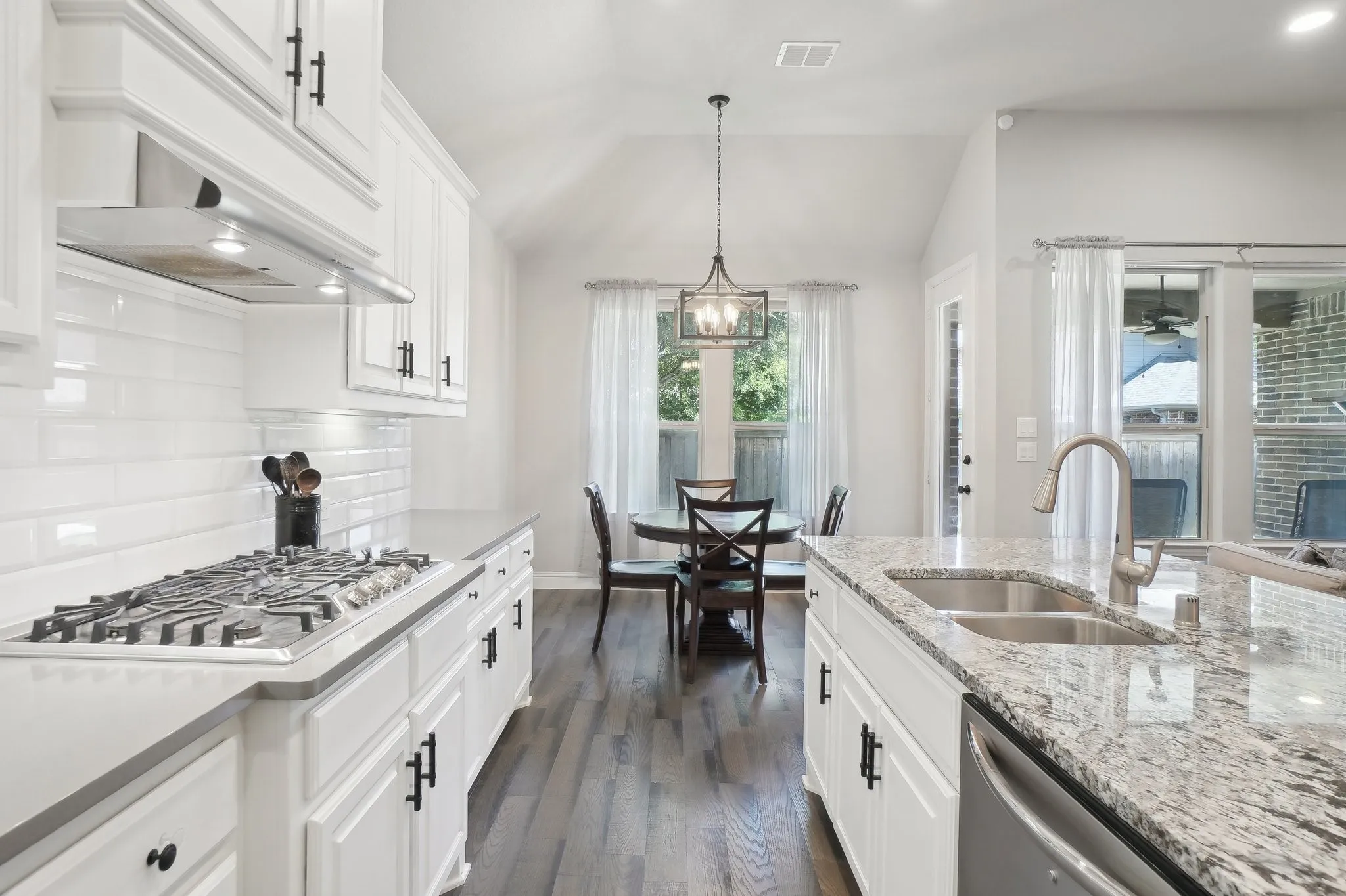 Kitchen with white cabinets, dark wood finished floors, light stone counters, stainless steel appliances, and vaulted ceiling