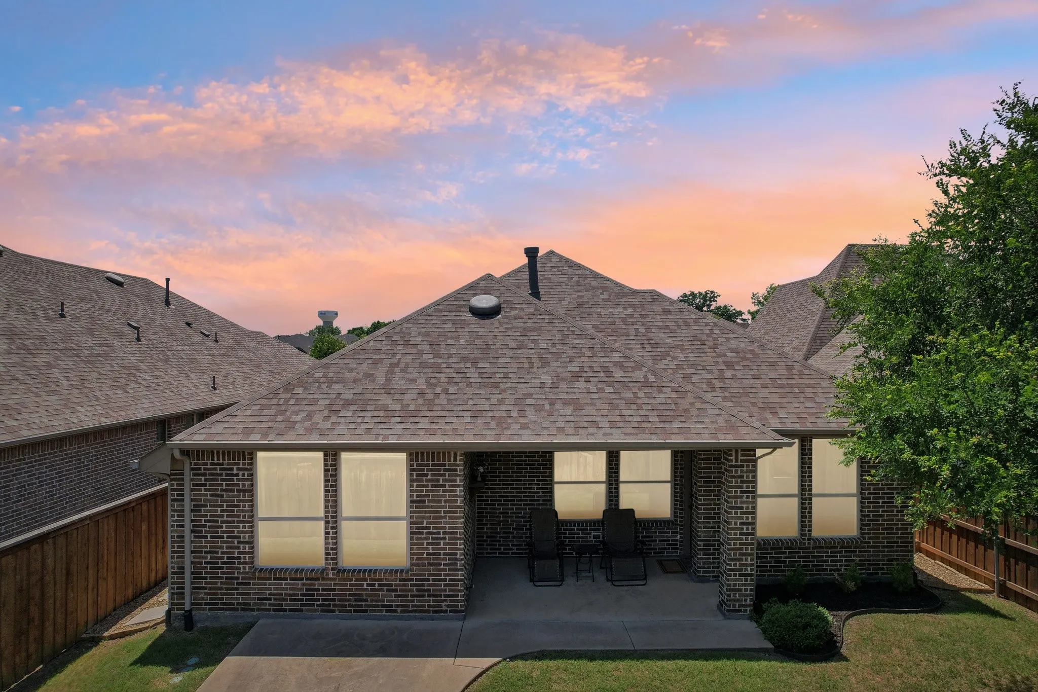 Back of house at dusk featuring a fenced backyard, brick siding, and roof with shingles