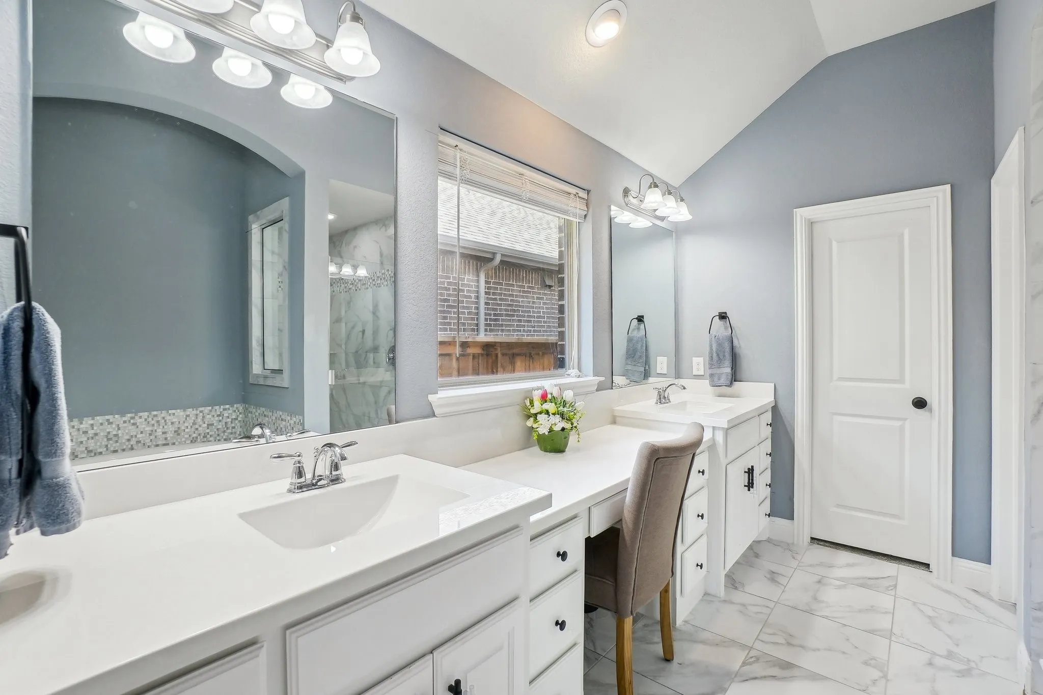 Full bath featuring double vanity, light marble finish flooring, lofted ceiling, and a marble finish shower