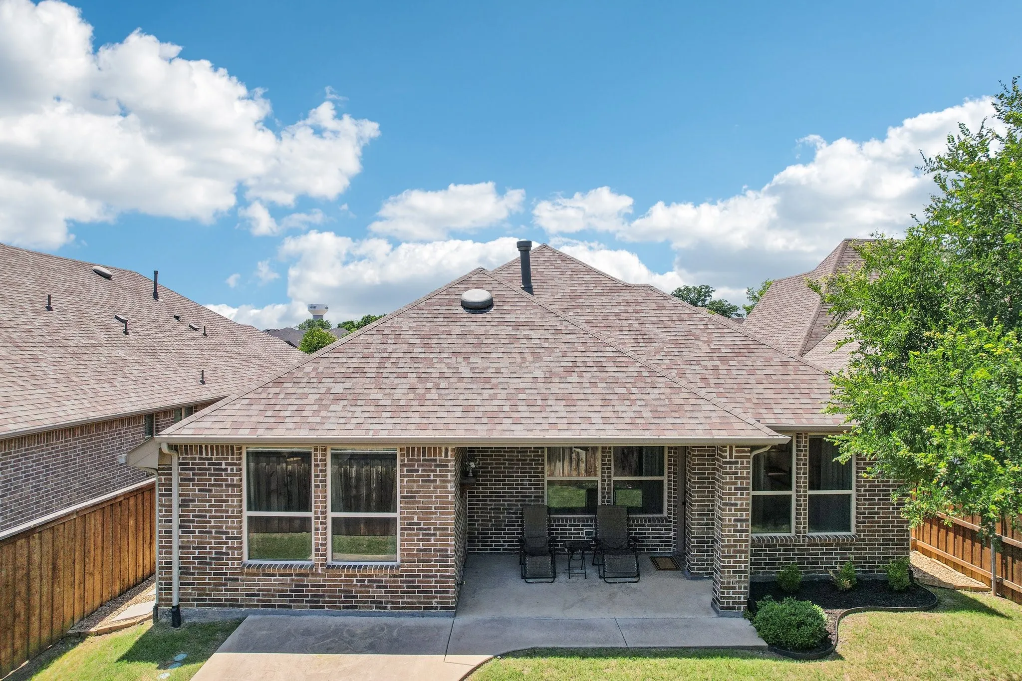 Rear view of property with a fenced backyard, roof with shingles, brick siding, and a patio area