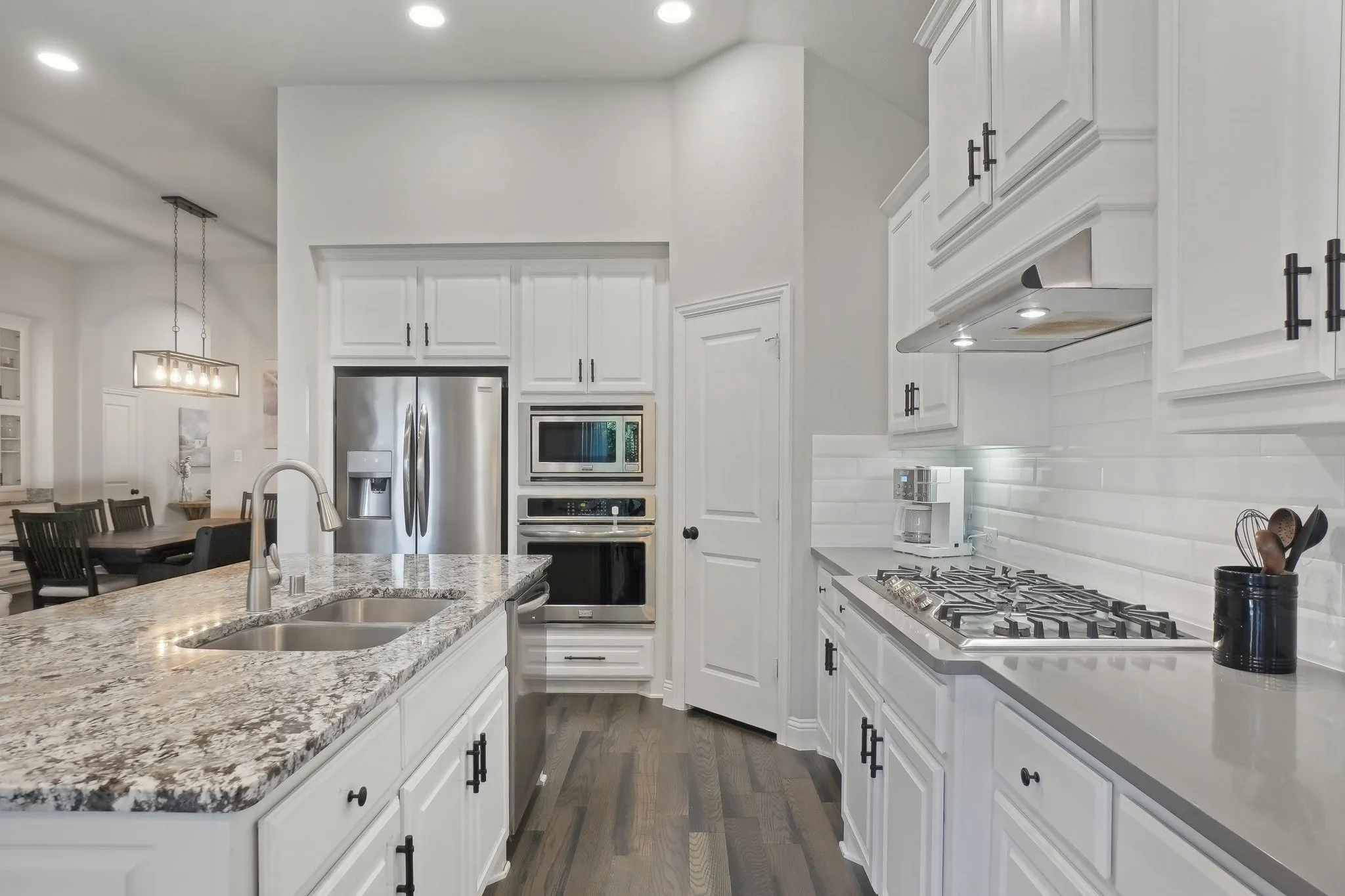 Kitchen featuring light stone countertops, white cabinetry, stainless steel appliances, decorative light fixtures, and dark wood-type flooring