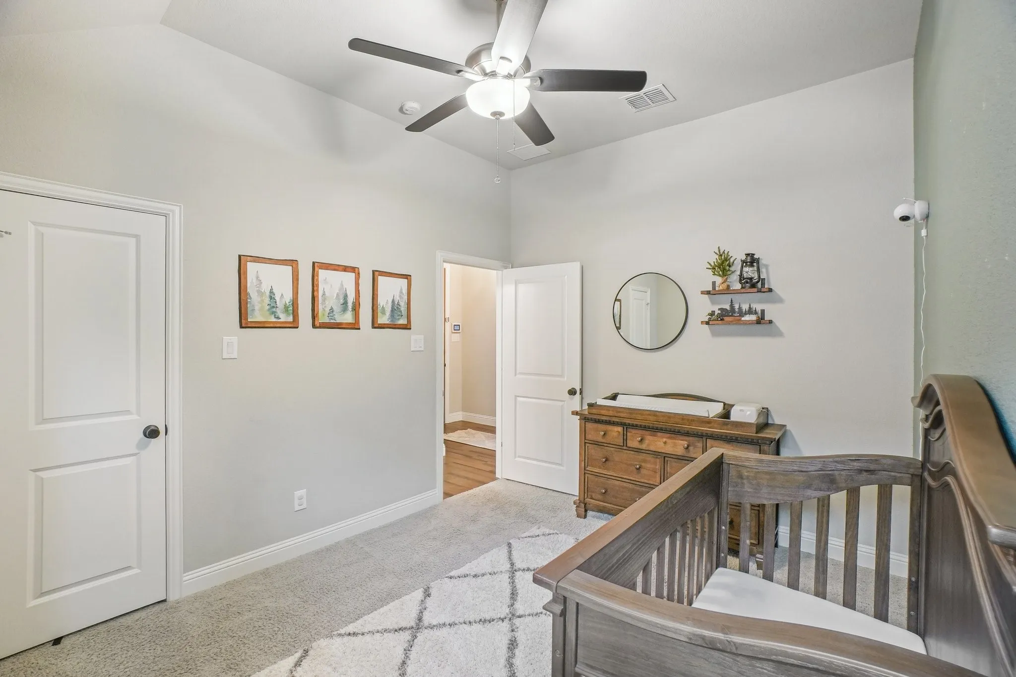 Bedroom with a nursery area, light colored carpet, and ceiling fan