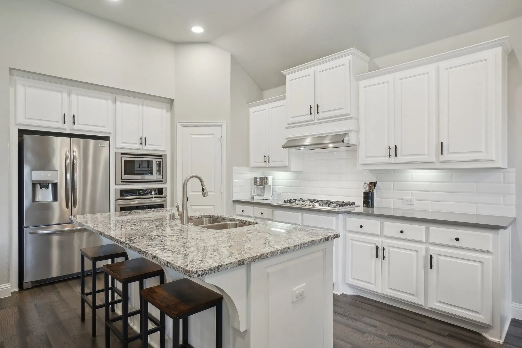 Kitchen with stainless steel appliances, light stone counters, white cabinetry, dark wood-style flooring, and lofted ceiling