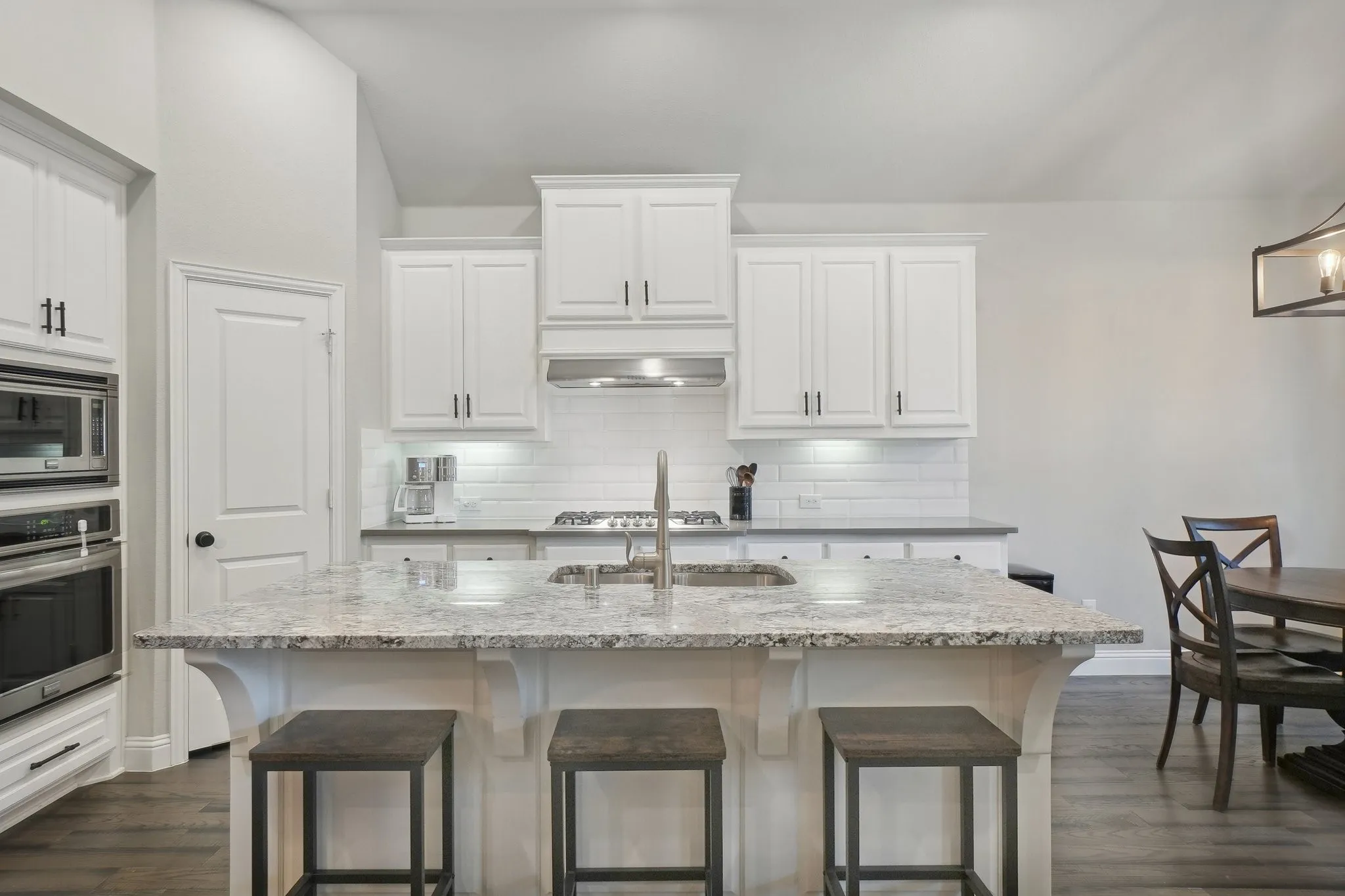 Kitchen featuring light stone counters, stainless steel appliances, a kitchen breakfast bar, an island with sink, and dark wood-style floors