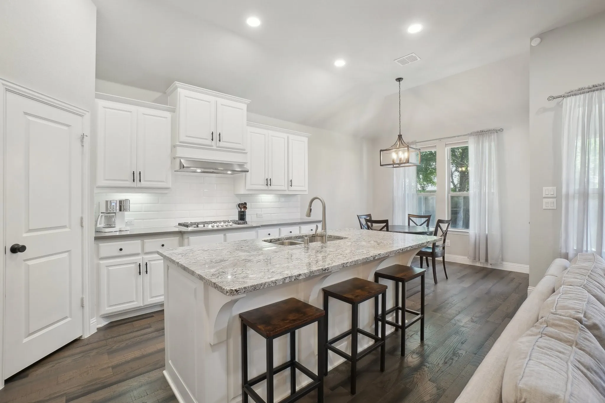Kitchen with a kitchen island with sink, vaulted ceiling, white cabinetry, light stone countertops, and a kitchen breakfast bar