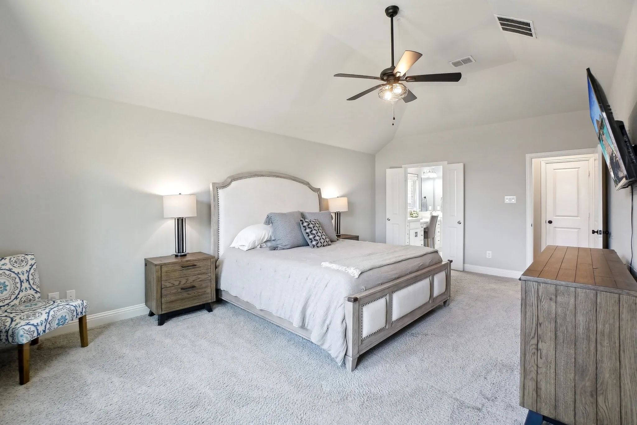 Bedroom with light carpet, a ceiling fan, vaulted ceiling, and ensuite bath
